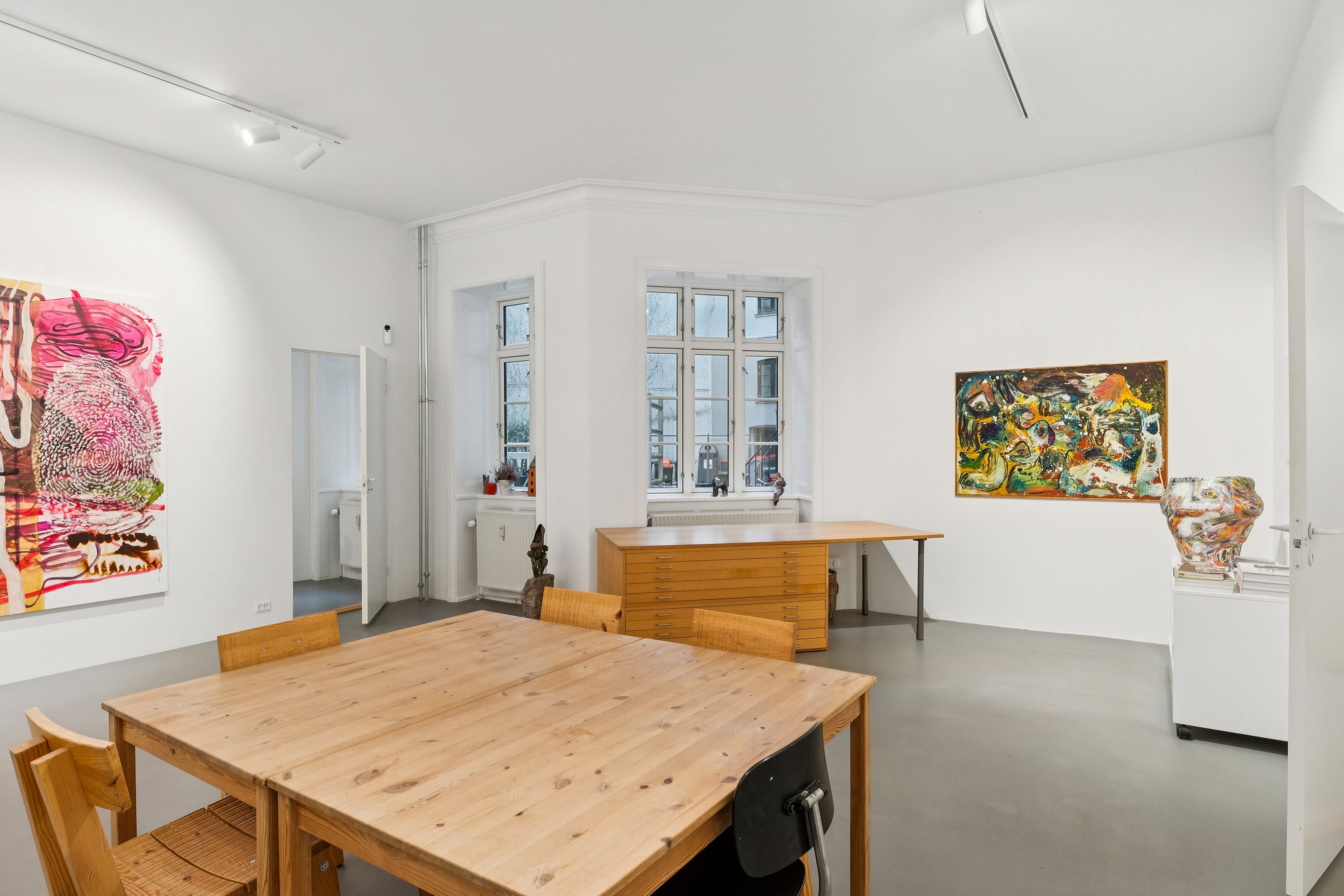 En minimalistisk indretning med en stor træbord og lysestole samt to malerier på væggen og en figur på gulvet