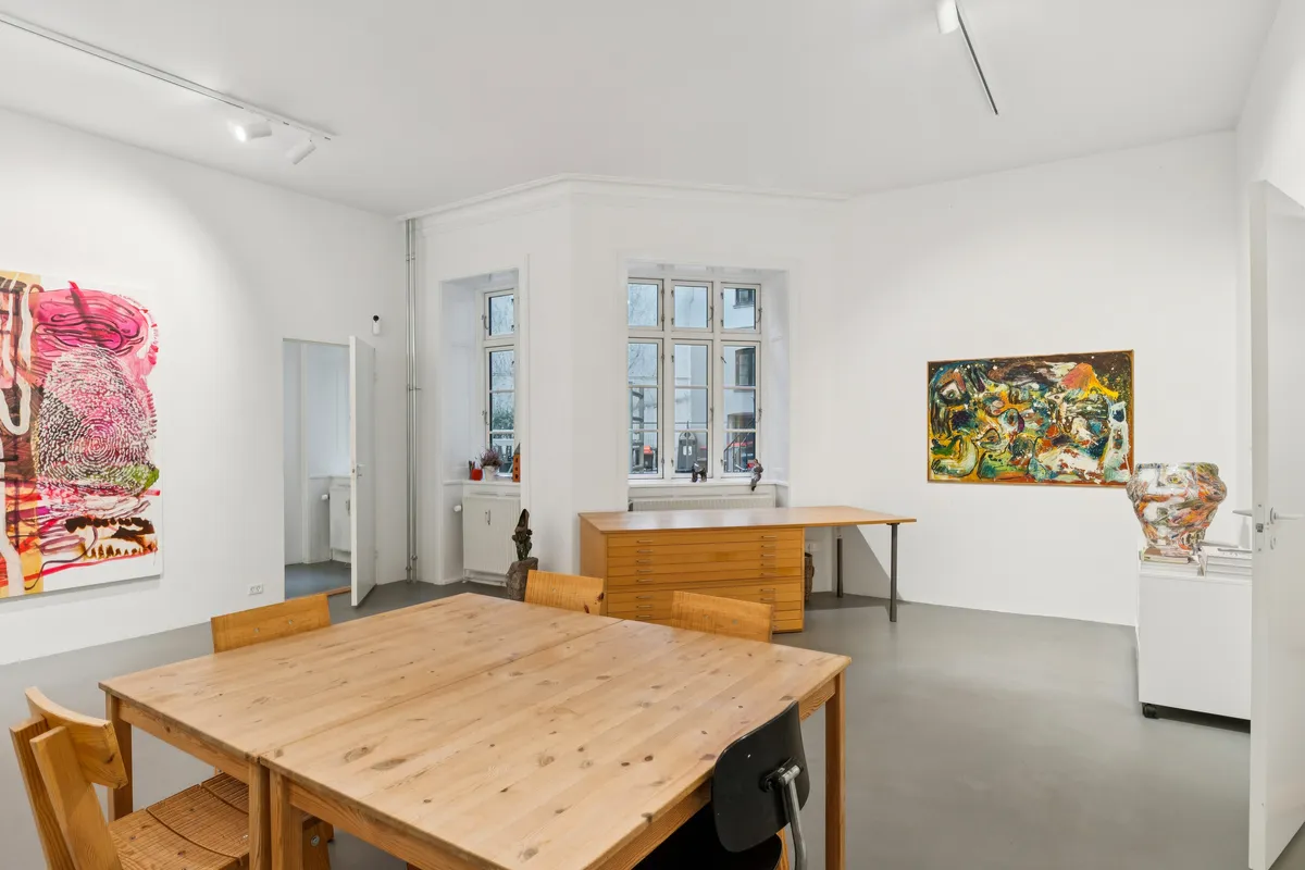 En minimalistisk indretning med en stor træbord og lysestole samt to malerier på væggen og en figur på gulvet