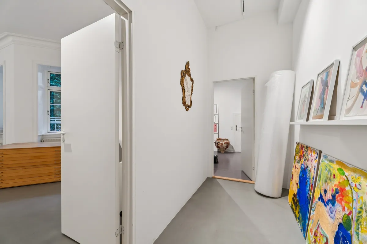 Hvidt rum med malerier på væggen og åbne døre. Møbler og vinduer. Malerier og en stor rolle papir på væggen.