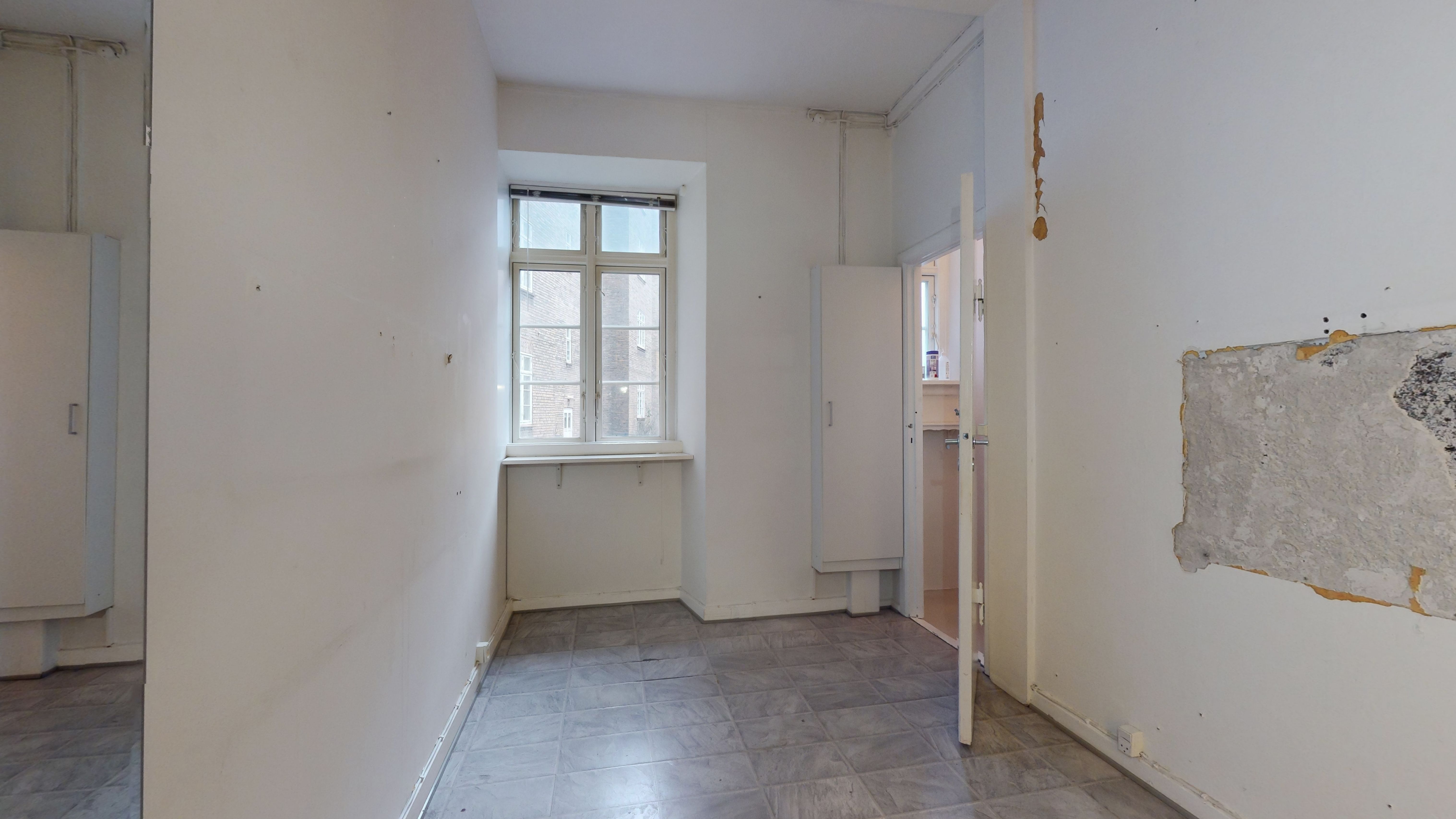 Kort korridor med hvide vægge og gulvtæppe, åben dør og vindue med gardiner samt opdelt loft.