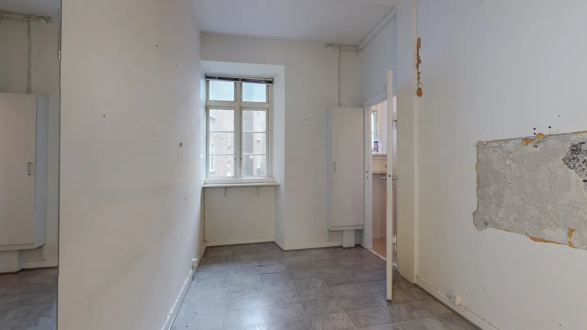 Kort korridor med hvide vægge og gulvtæppe, åben dør og vindue med gardiner samt opdelt loft.