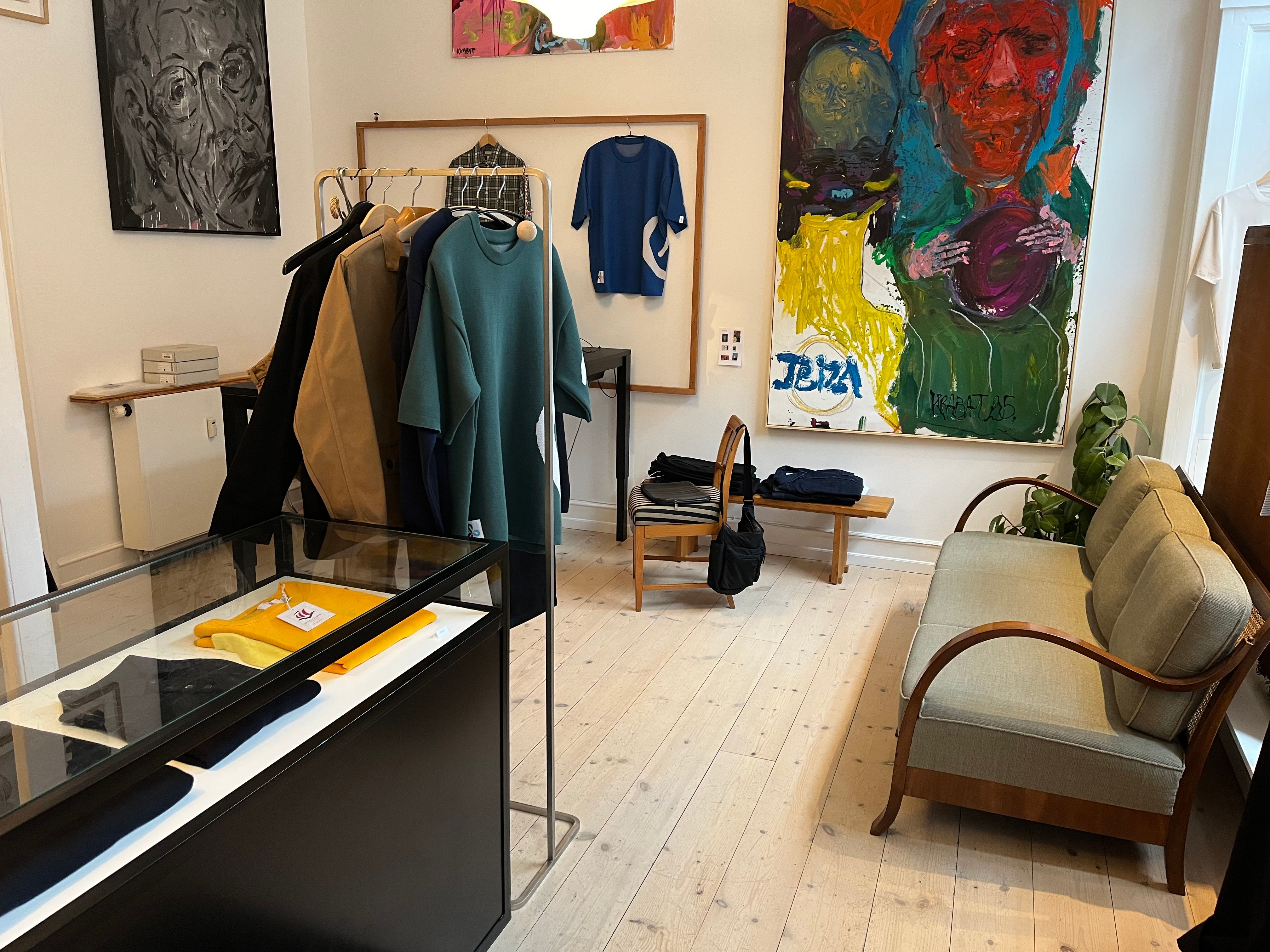 Et moderne interiør med tøj i garderobe, kunstværker og møbler, der inkluderer en sofa og stole på en trægulv med plante ved siden af