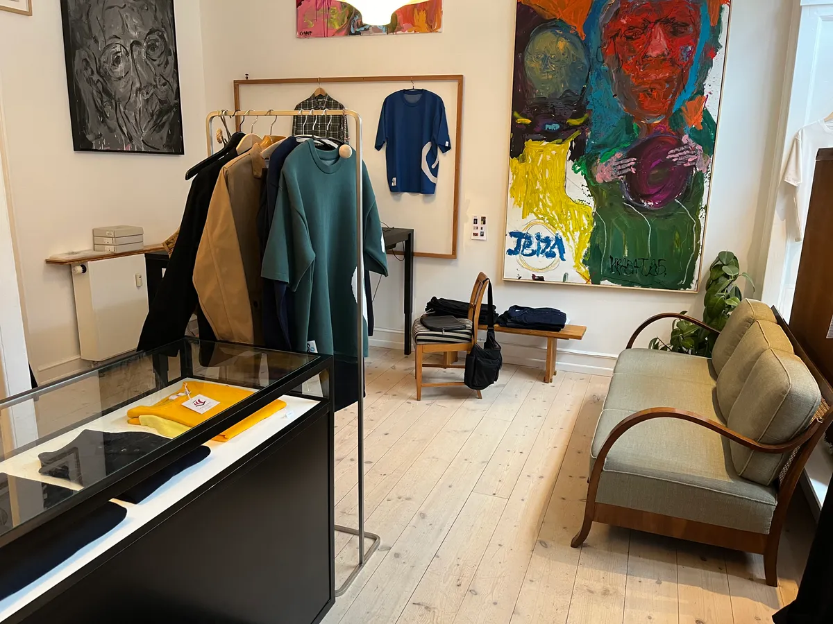 Et moderne interiør med tøj i garderobe, kunstværker og møbler, der inkluderer en sofa og stole på en trægulv med plante ved siden af