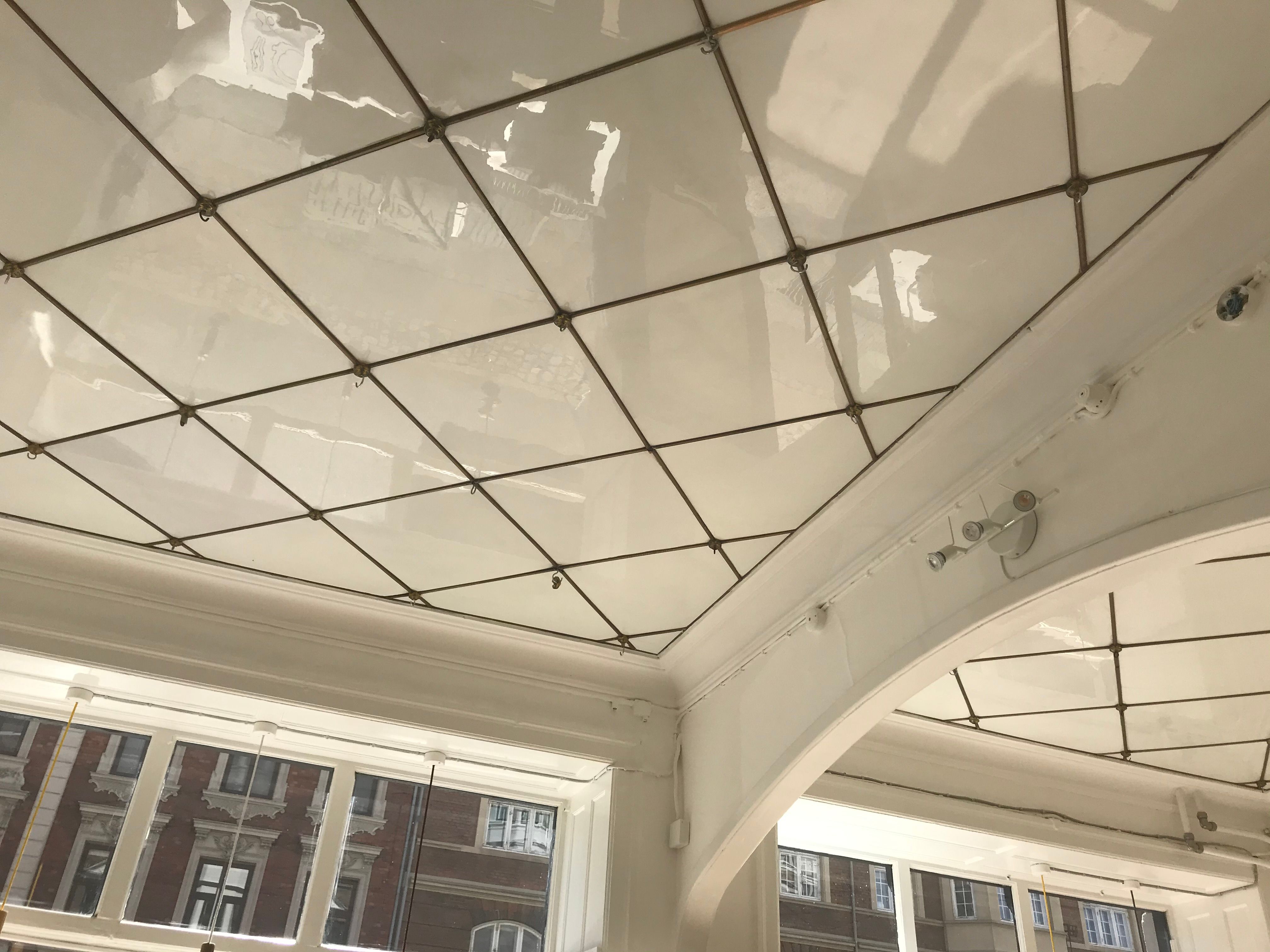 Hvidt loft med rektangulært mønster og metalbånd på lyserødt bygningsudsnit med flere vinduer og glaspartier