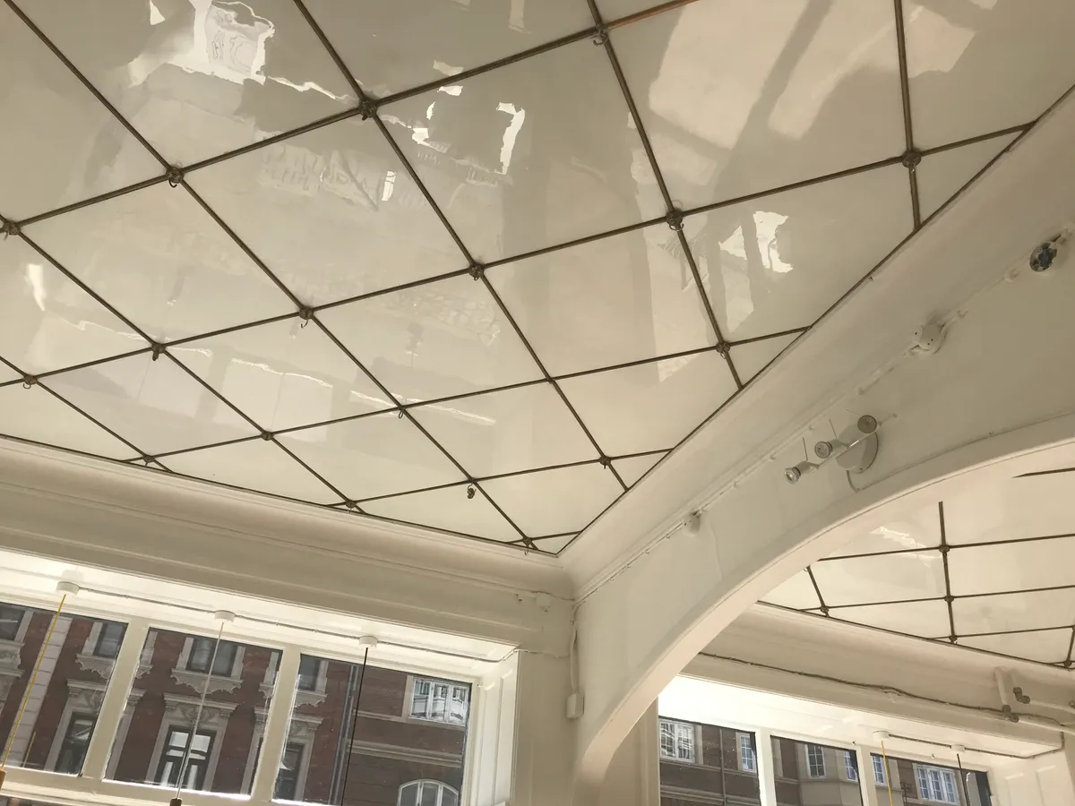 Hvidt loft med rektangulært mønster og metalbånd på lyserødt bygningsudsnit med flere vinduer og glaspartier