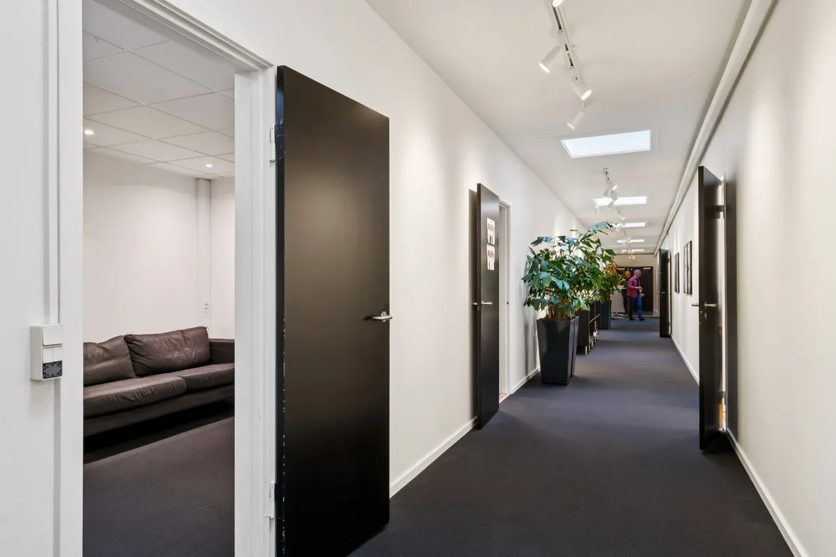 Kontor med indgangsparti, sofa, plante og to elevatorer i hvid og sort. Gulvet er dækket med sort gulvtæppe og der er hvide vægge