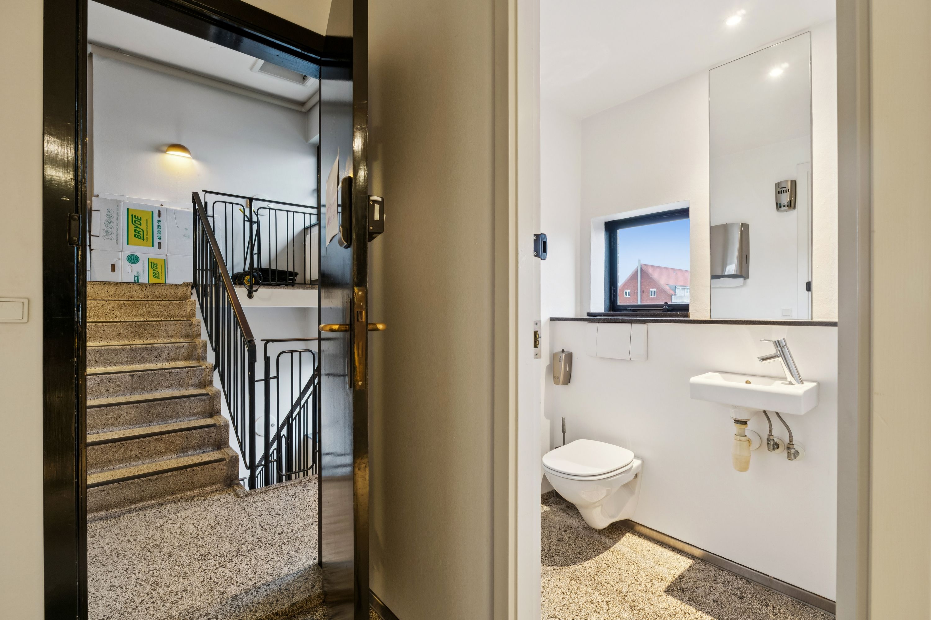 Kontor med toilet og spejl i Charlottenlund. Væggene er hvide, og der er en håndvask med vandhaner og et toilet. Stairs med håndtag og stige.