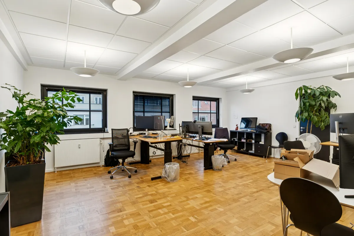 Kontor til leje i Charlottenlund med moderne udstyrede arbejdsområder, højloftede rum, store vinduer og flot indretning. Kontor med trægulve, lyse loftslamper og lysegrå vægge