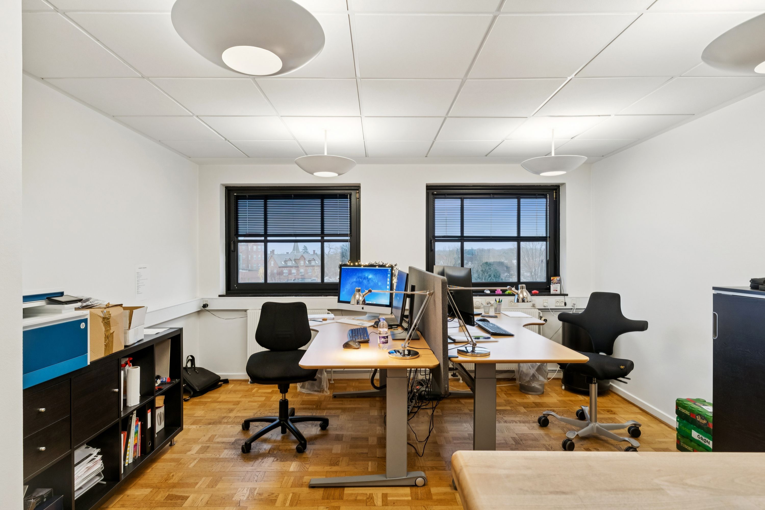 Kontorrum med skrivebord, computer, skrivebordslampe og kontorstole. Moderne og velholdt kontorlokaler med højt til loftet og vinduer. Lys og rummelige kontorer i en flot og velholdt ejendom