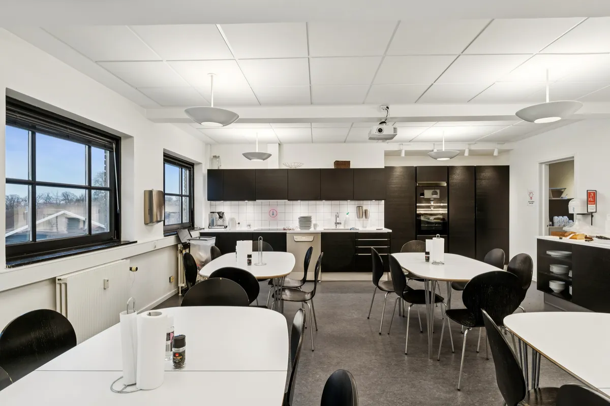 Køkken med hvide vægge, runde borde, moderne møbler, hængende lysekroner og projektor til præsentationer og møder