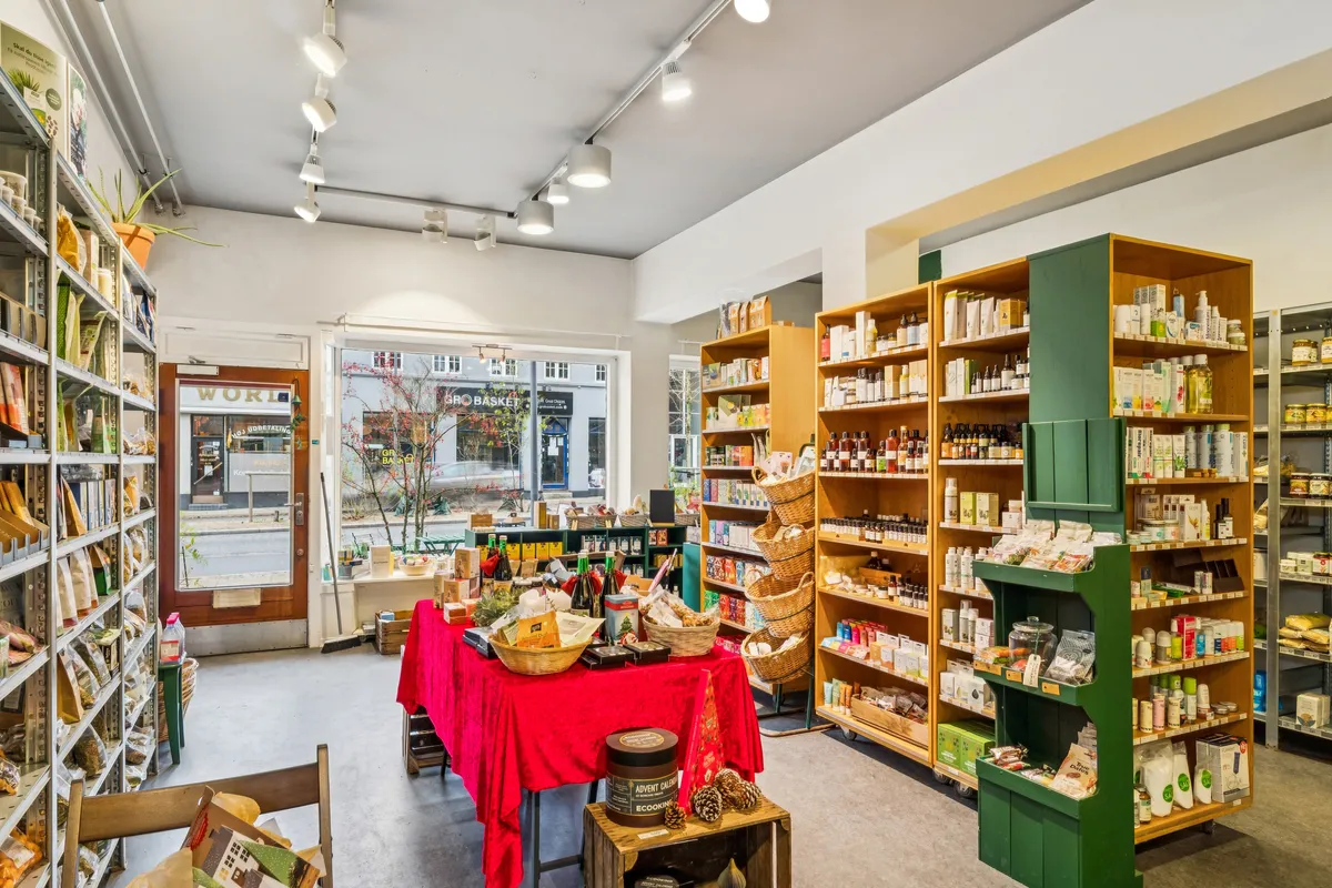 Indvendørs i en moderne økologisk butik med reoler fyldt med diverse produkter, spredt med plantepot og en rødt dækket stol med adventskalender