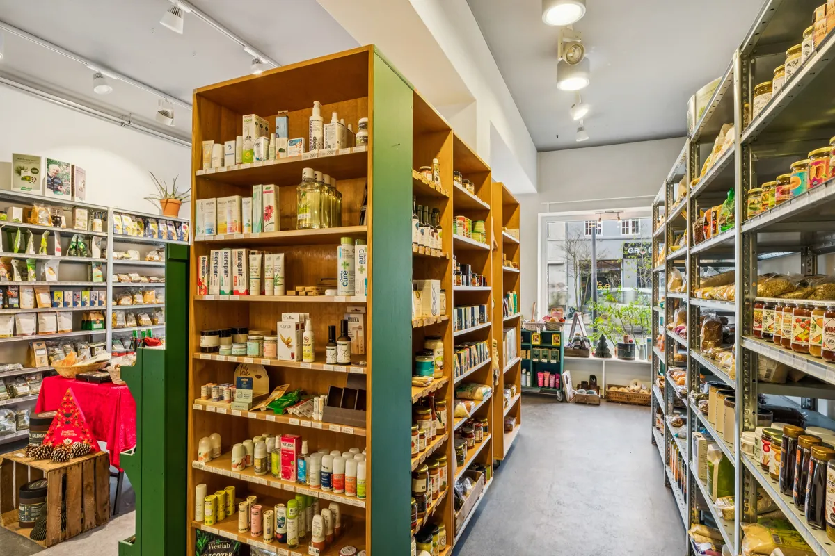 Søborg butik med flere hylder med olier, urtepræparater og konserver. Lys gulv og lysekroner i loftet. Udsigt til gade og planter i vindue.