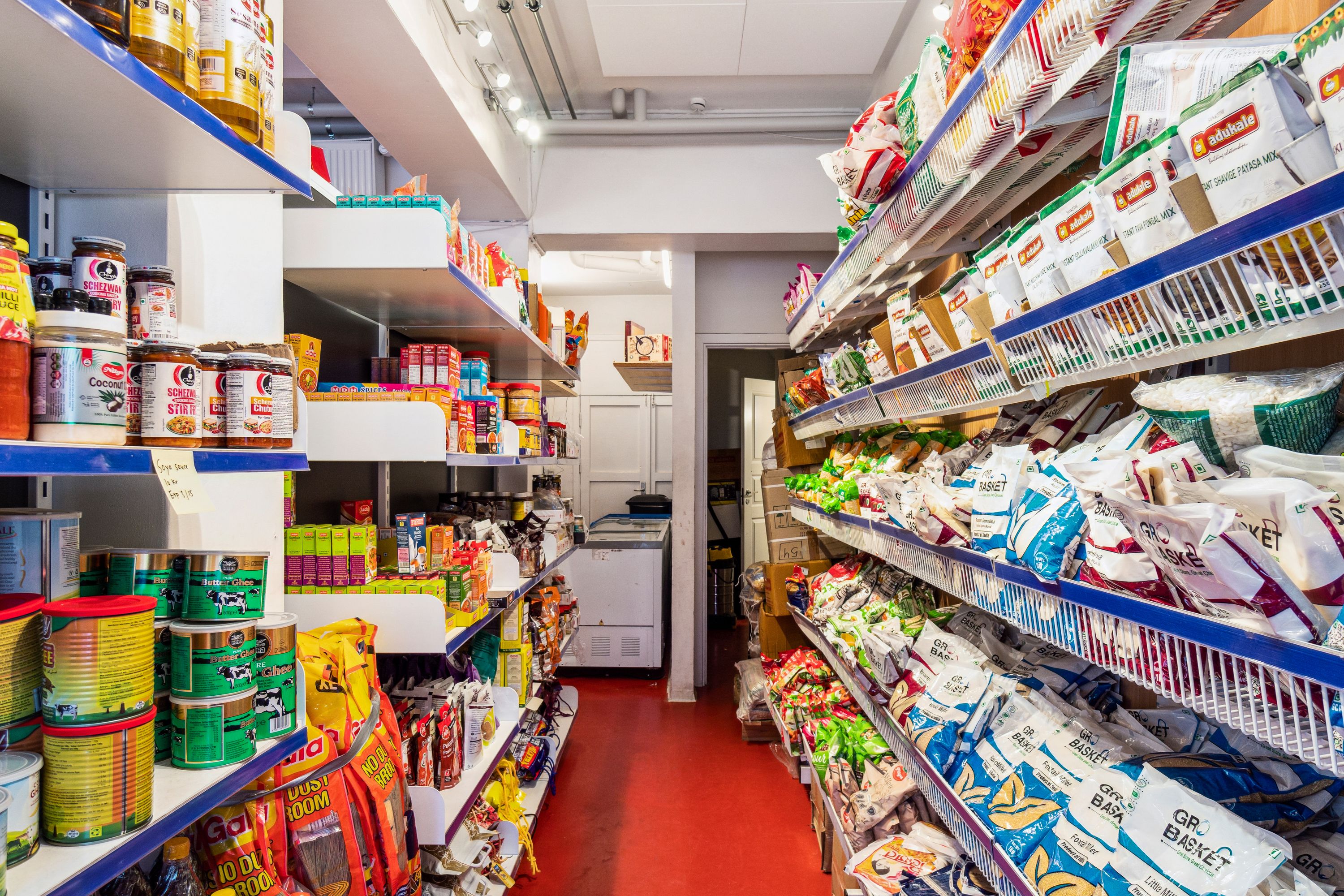 En fyldt specialbutik med krydderier og snacks på hylderne og rødt gulv. Høje hylder med forskellige snacks og krydderier. Butikken har flere hylder med forskellige produkter og krydderier.