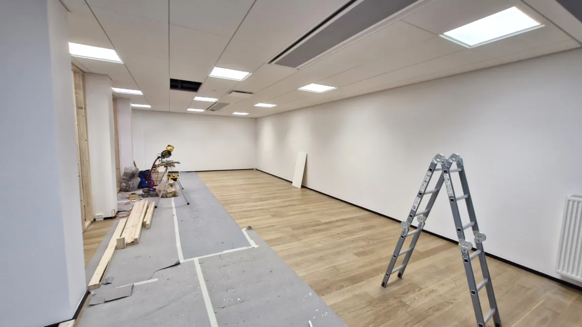 Tomten er under renovering med træbjælker og værktøj samt hvidt vægpanel og lysekroner og en stige i enden af rummet