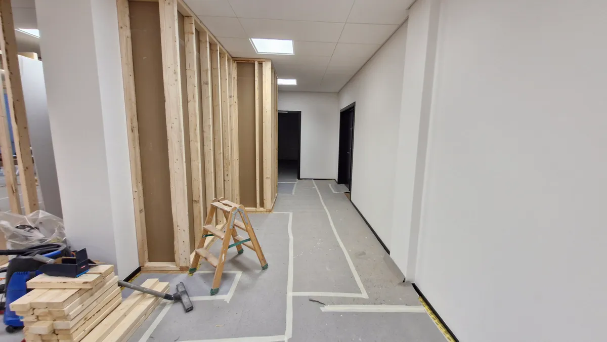 Kortsnoret gang med træstativ og byggematerialer i en renoveret lejlighed. Møbler og gulv er endnu ikke færdiggjort