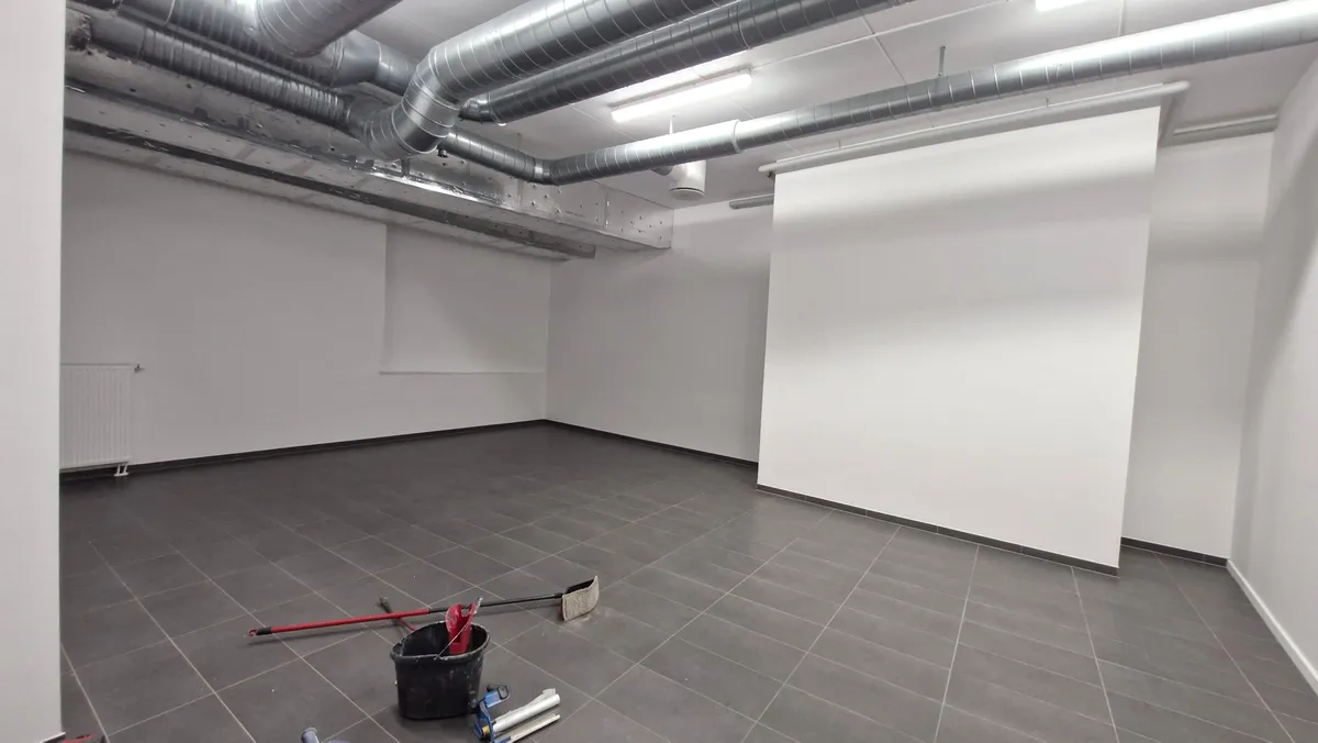 Rummelige lokaler med moderne lofter og møbler. Til venstre er en radiator og rengulvet. Rengøringsudstyr står på gulvet.