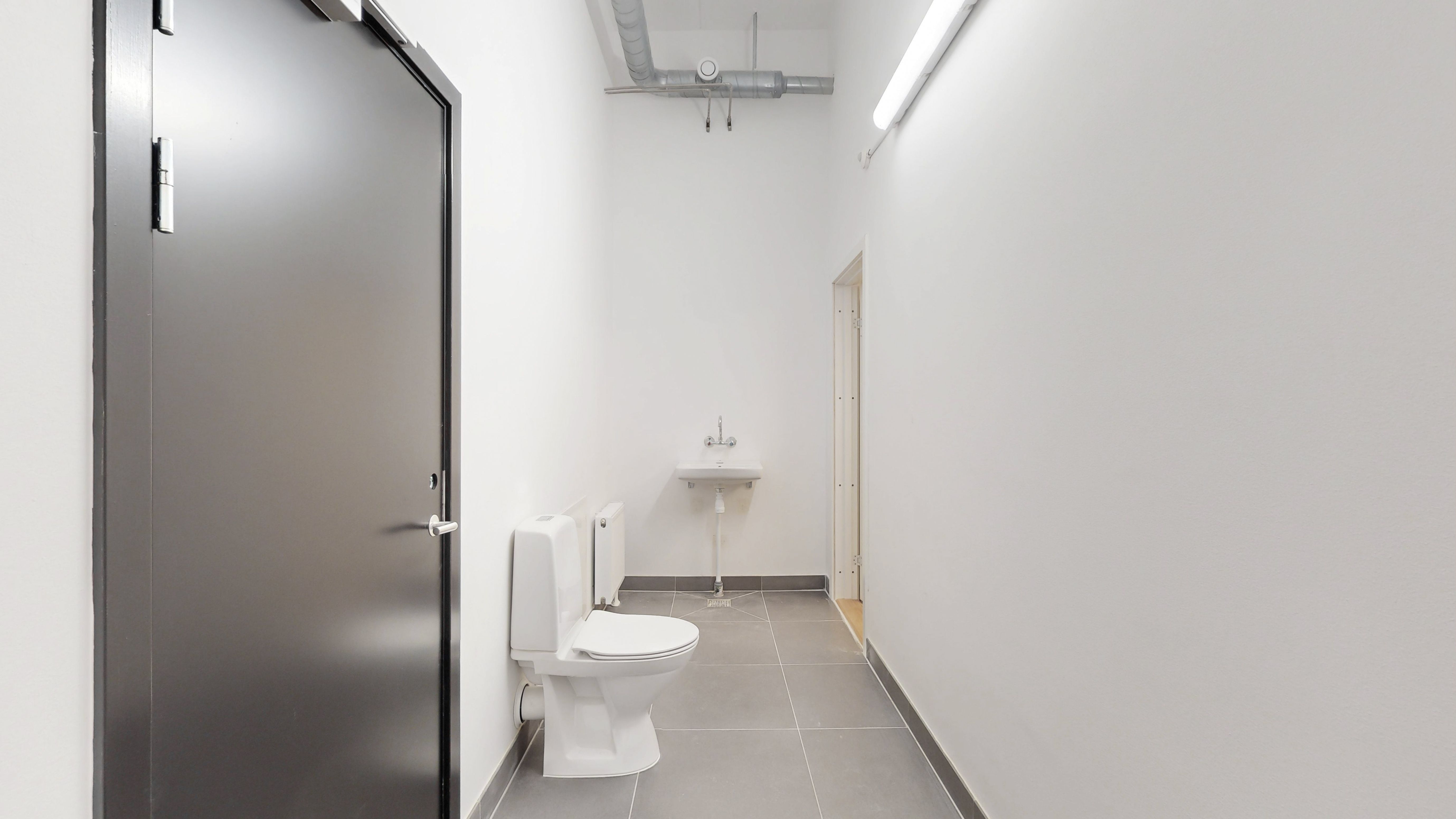 Rent og rent toilet med en hvid toilet med hvidt sæde og et hvidt vask med håndvask samt gulvtøj i en hvid og grå farve.