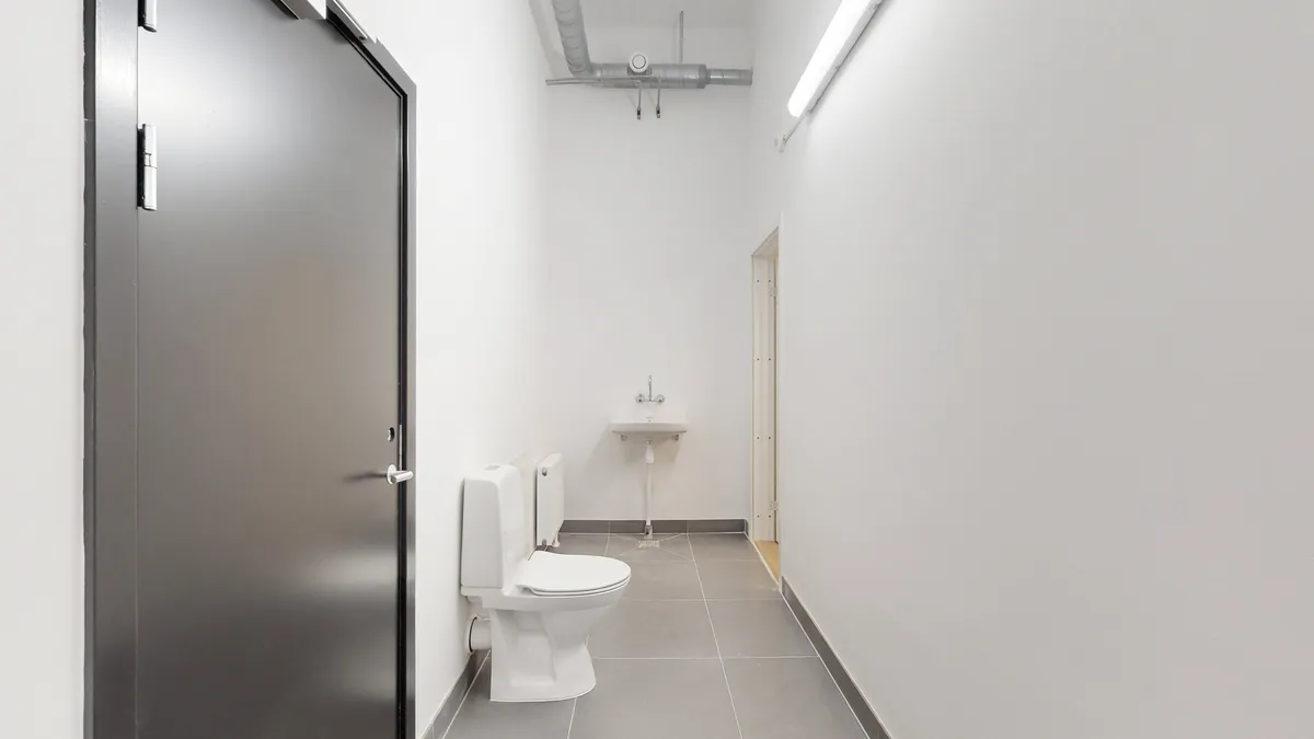 Rent og rent toilet med en hvid toilet med hvidt sæde og et hvidt vask med håndvask samt gulvtøj i en hvid og grå farve.