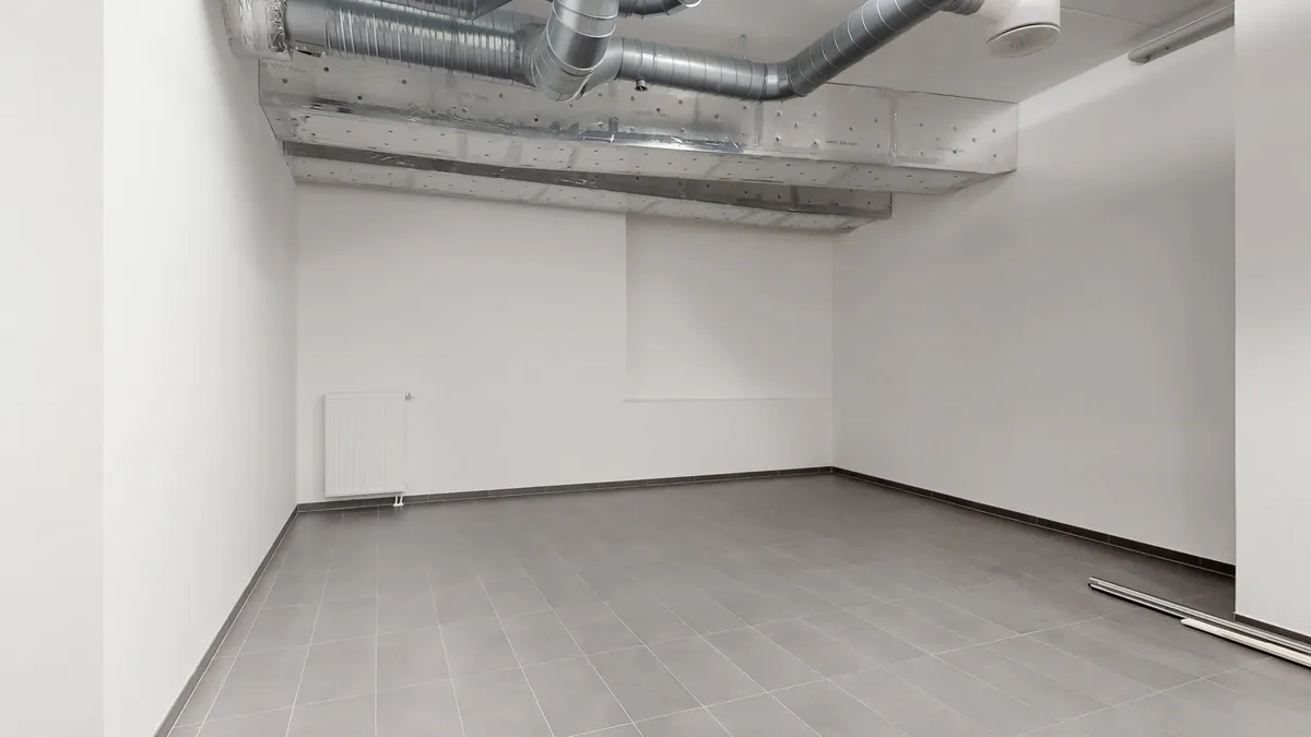 En stor, tom lejlighed med hvidvaskede vægge og lysegrå gulvfliser. Et større vinduesparti og lysekroner udgør det vigtigste udstyr i rummet