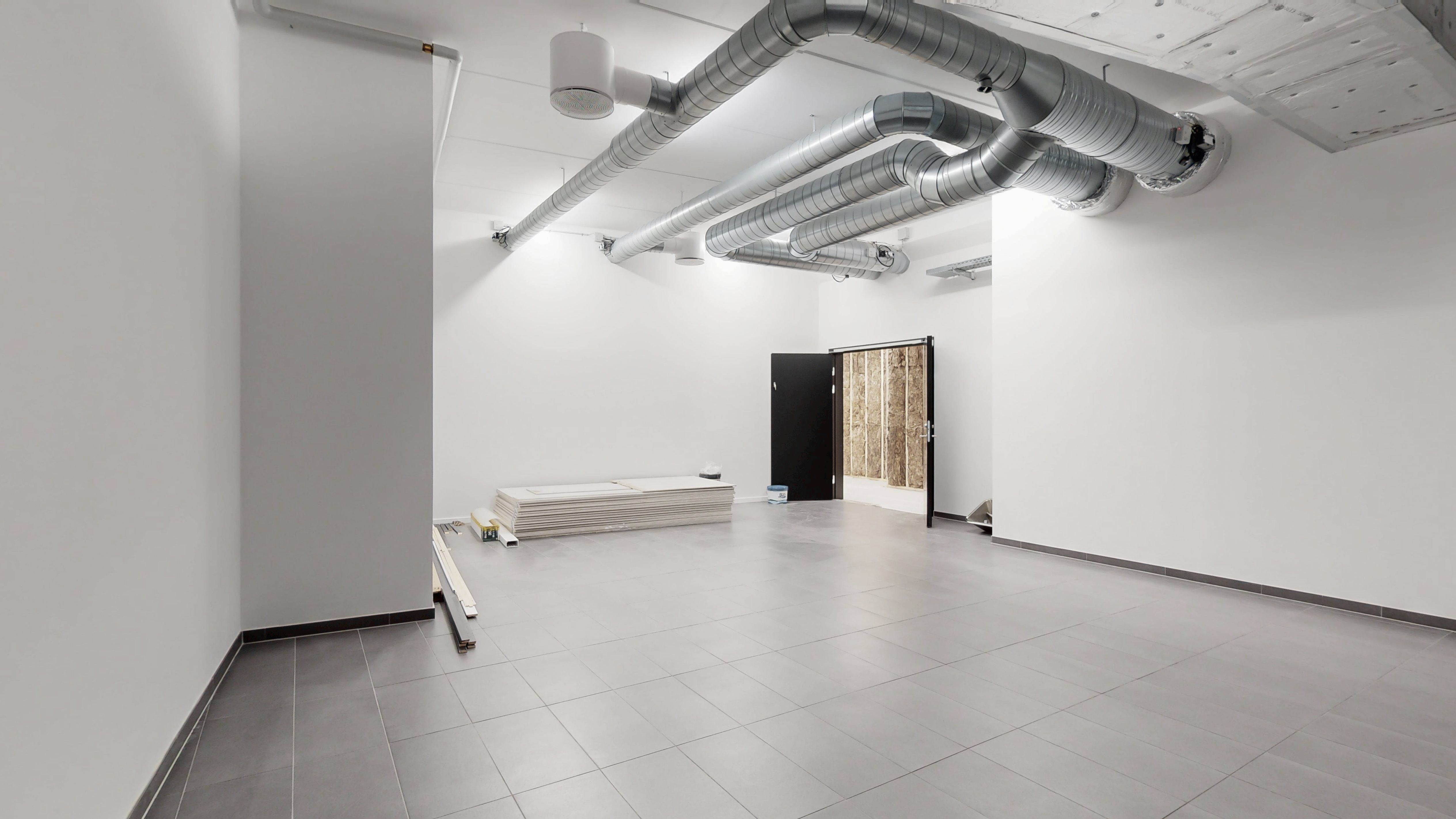 Ingen møbler og byggematerialer i det tomme rum med lysegule loftslampe. To vinduer med hvide rammer og sort dør i højre side.