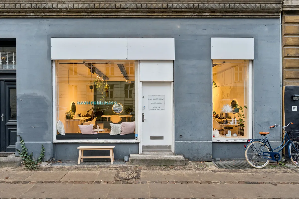 Lyst og moderne lejemål i København med butiksvindue og hvid dør, hvor der er udsat tæpper og puder til salg