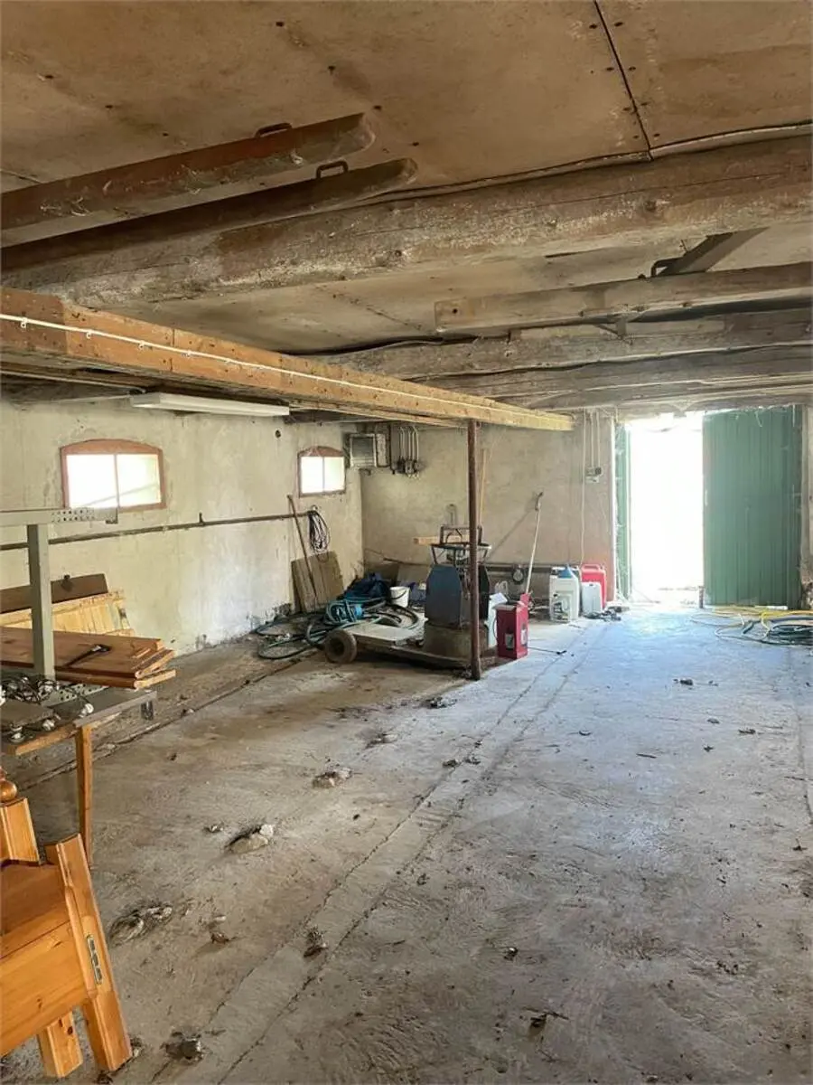 Lagerhal med jordgulv og vinduer, værktøj og materialer er fordelt rundt, og der er en grøn dør til udgang