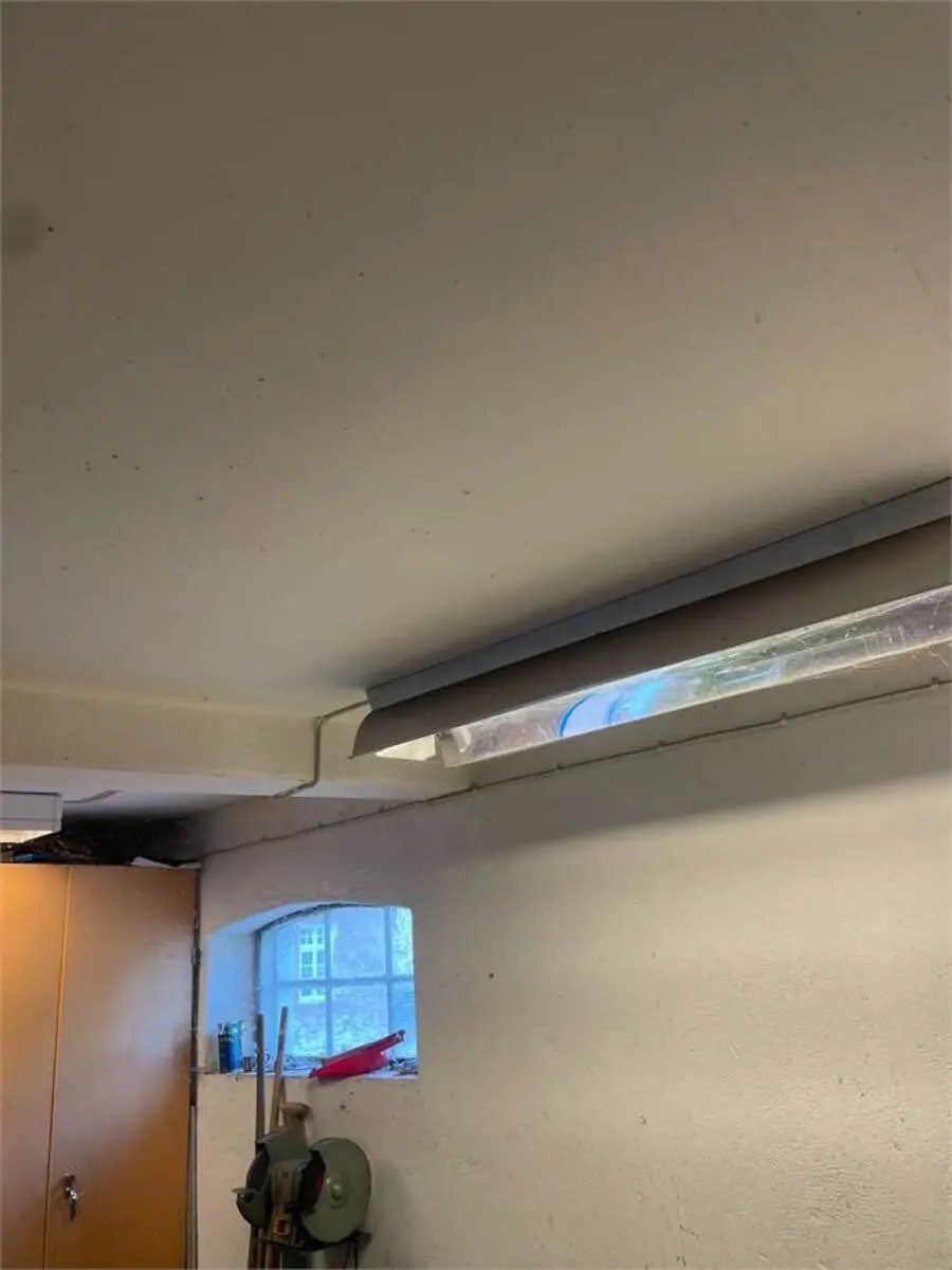 Garage med lys, vinduesbue, gulvmonteret skraper, rød plastbeholder, rødt bælte, brædder og vinduesglas. Lagerlokale med loftsbjælke, trækabinet og loftsvinduesbue.