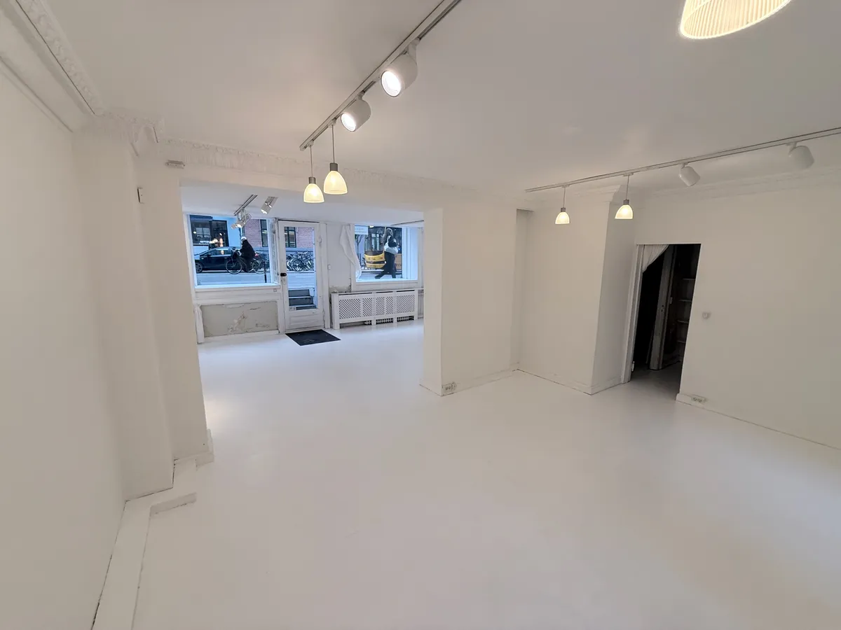 En stor, ren, hvid rum med flere indgange, lysekroner og vinduer med udsigt til gaden med biler og cyklister