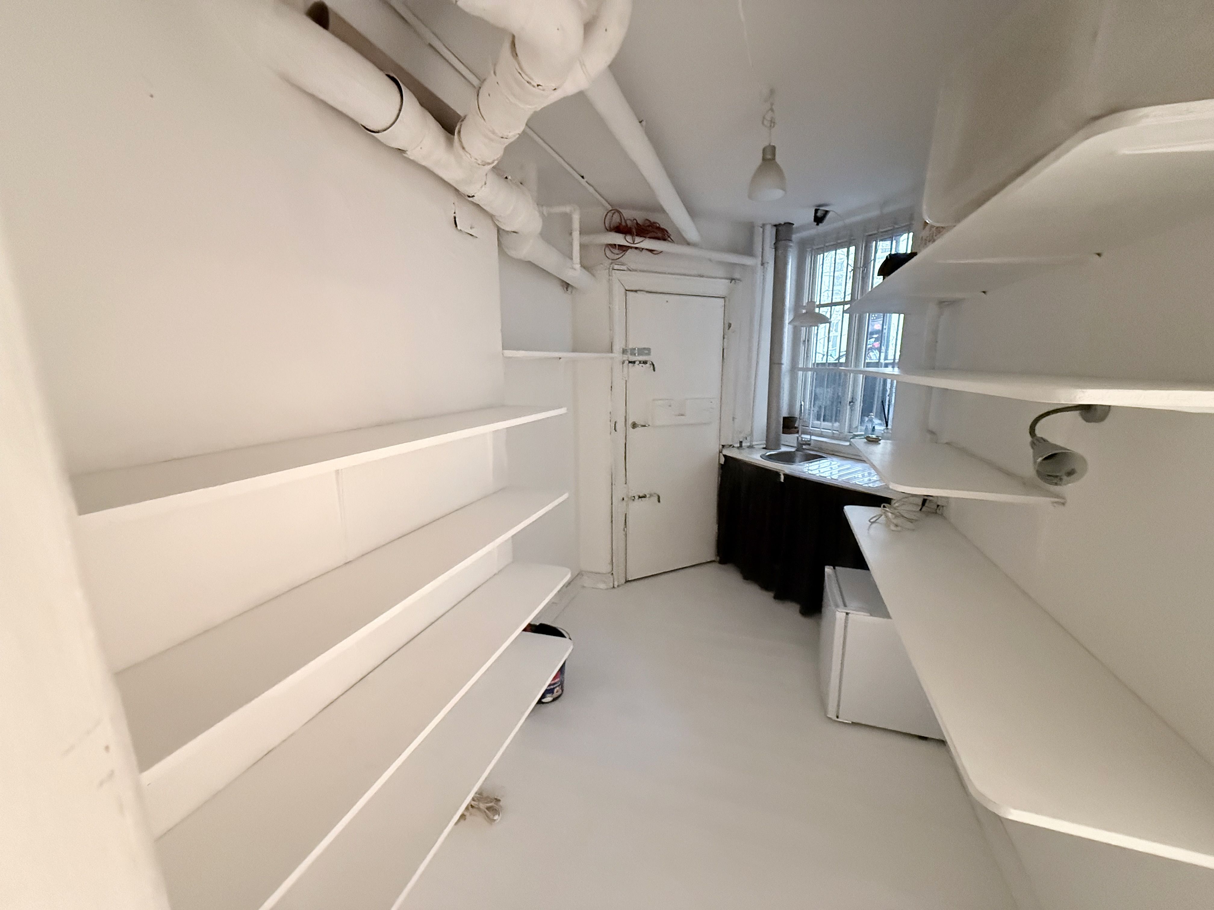 Et køkkenrum med hvide vægge, hvide hylder og lysekroner samt et åbent vindue med gardiner.