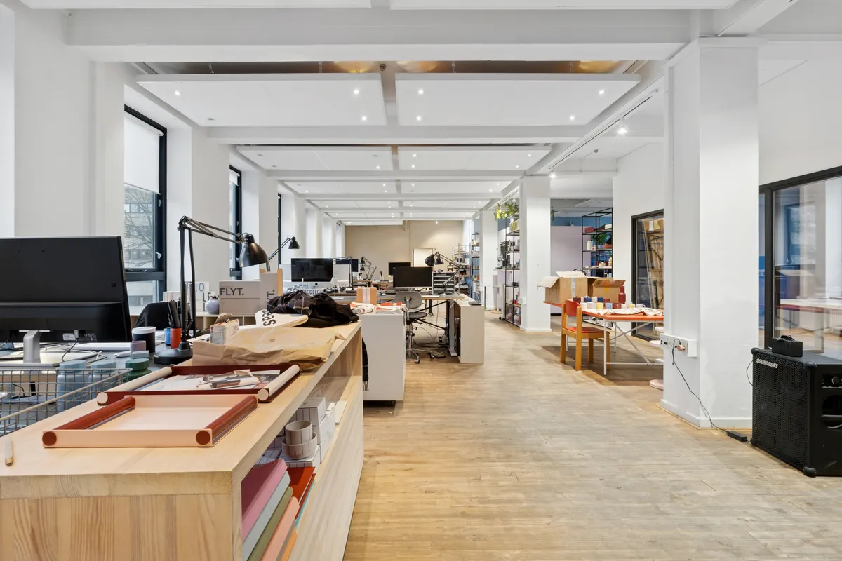 Kontor med computere, stole, skriveborde, lys, og møbler i en stor rummelig stue med højt loft og trægulve