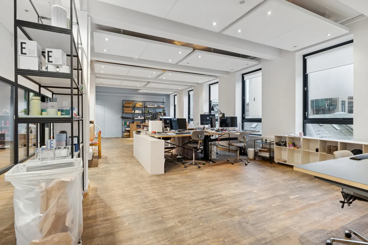 Storrumskontor med moderne indretning, trægulve, højt loft og vinduer med udsigt til byen