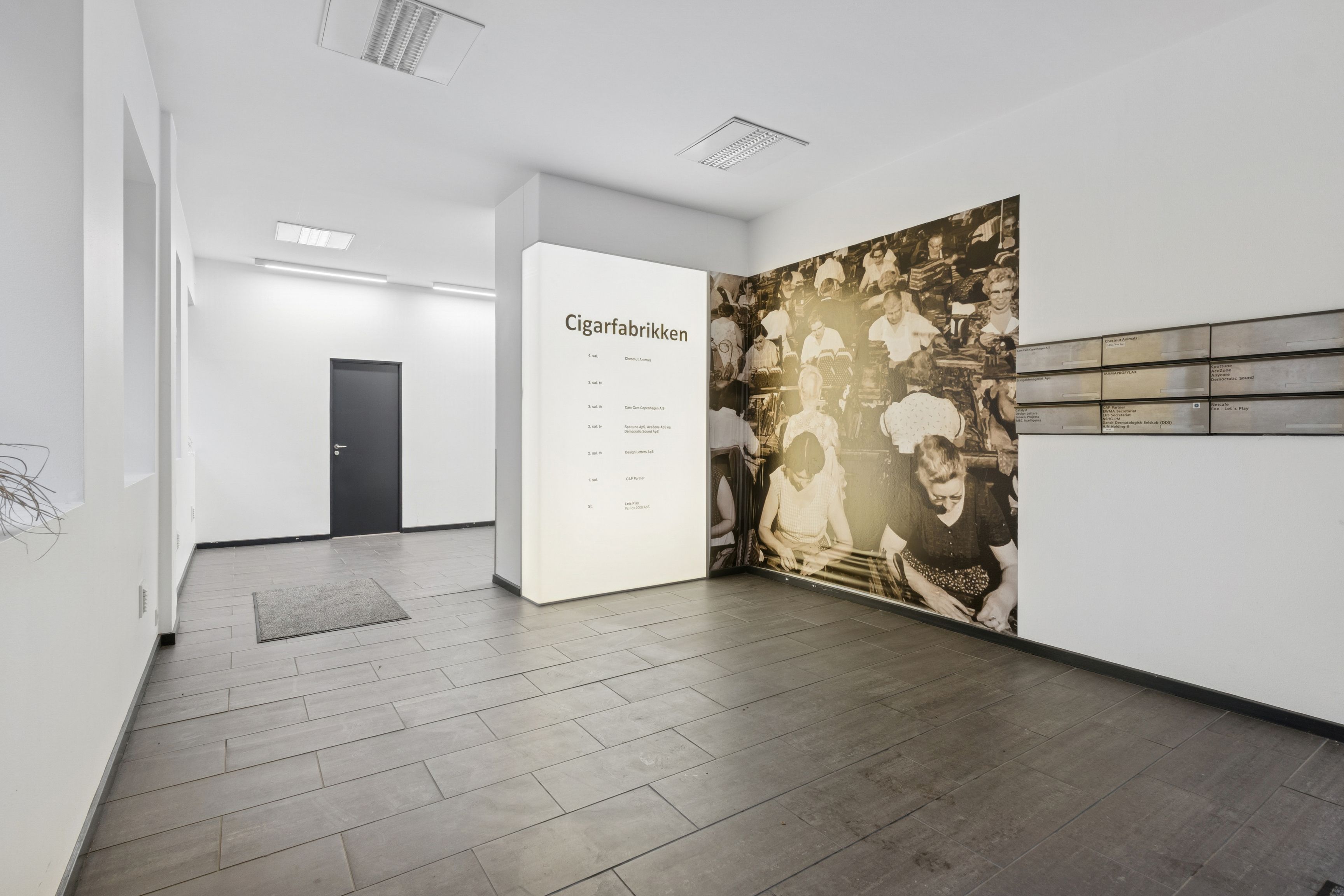 Store rum med højloft og gulvbeklædning i massivt træ. Loftventilation og tekst på væggen, der læser Cigarfabrikken.