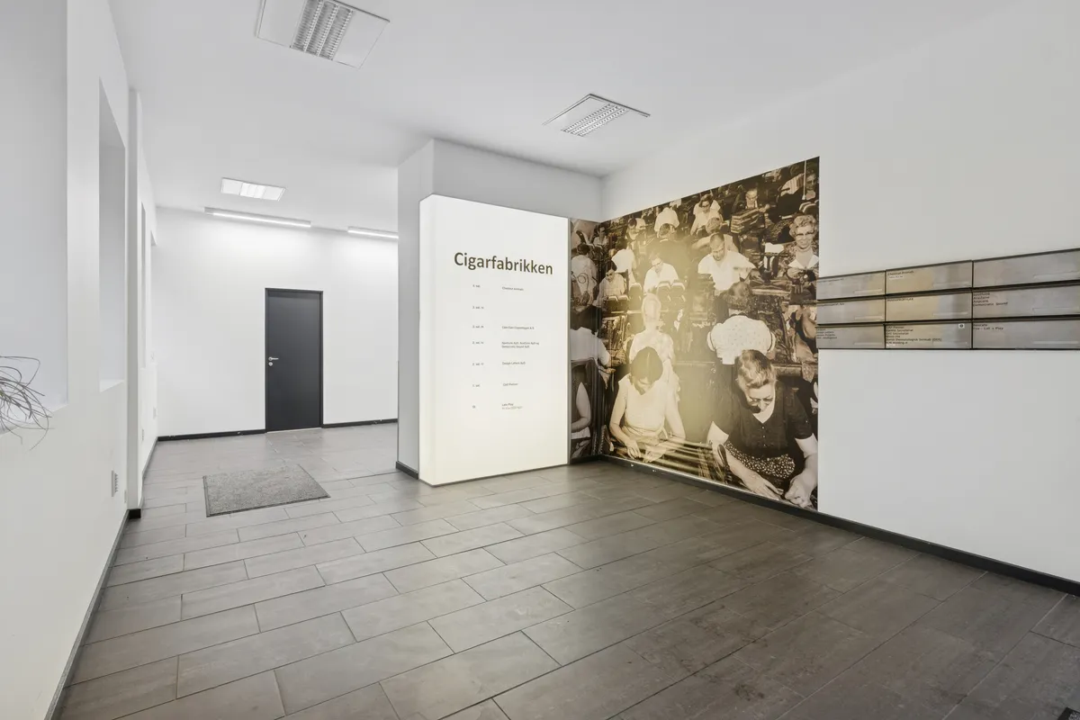Store rum med højloft og gulvbeklædning i massivt træ. Loftventilation og tekst på væggen, der læser Cigarfabrikken.
