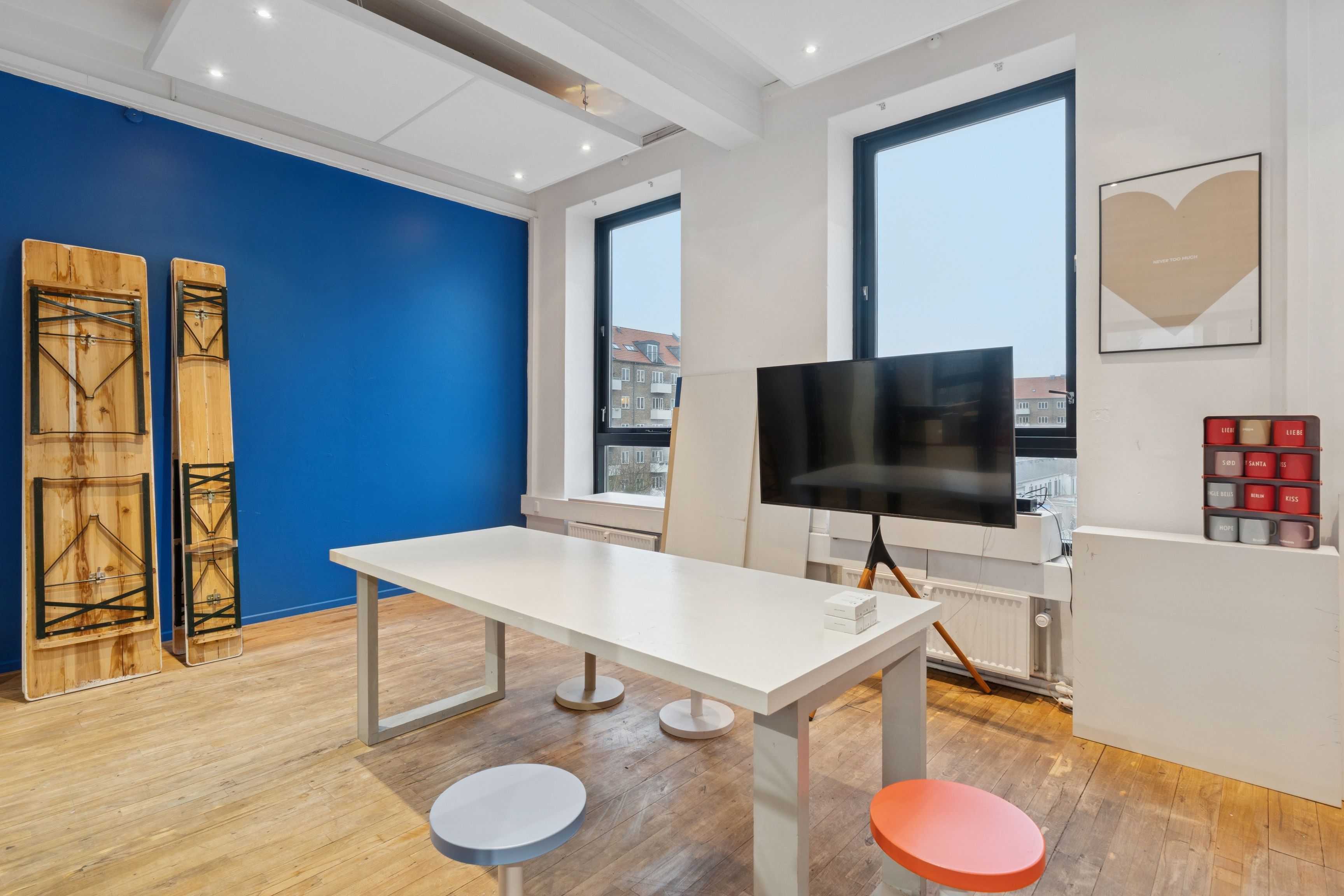 Billede af et stort kontor med lysegul væg og møbler i hvidt og lysebrunt, to stole, højt tv og loftsventilatorer samt et træbord med små bokse