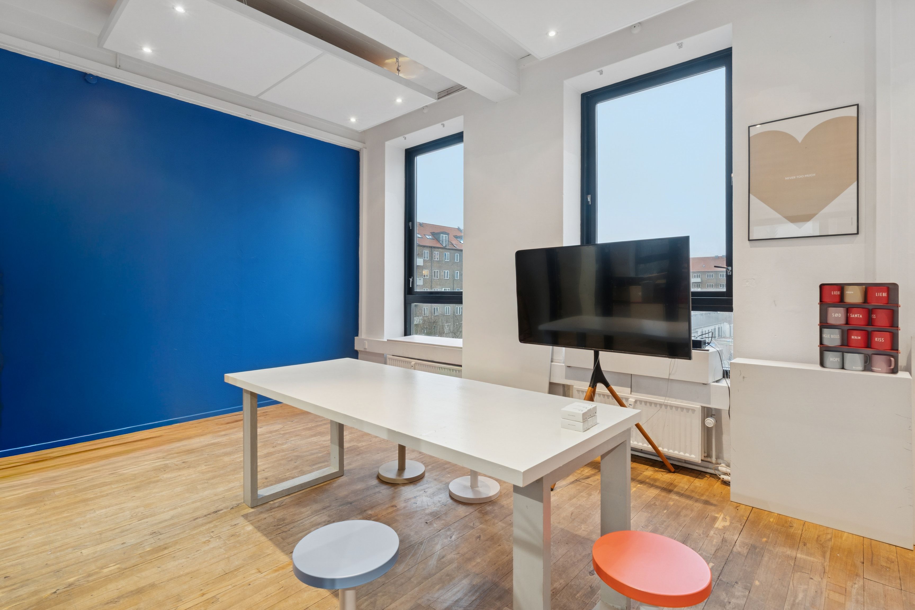 En stor rummelig stue med hvide vægge og gulv samt en stor blå væg og en stor sort tv-skærm samt to stole og en lang hvid bord