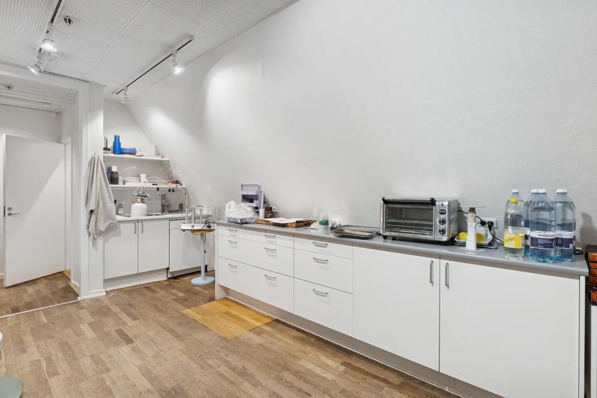 Stort hvidt køkken med lysekroner, hvide skabe, trægulv og lyseblå vægge. Køkken med moderne apparater, træbord, håndklæder og vandflaske på disken