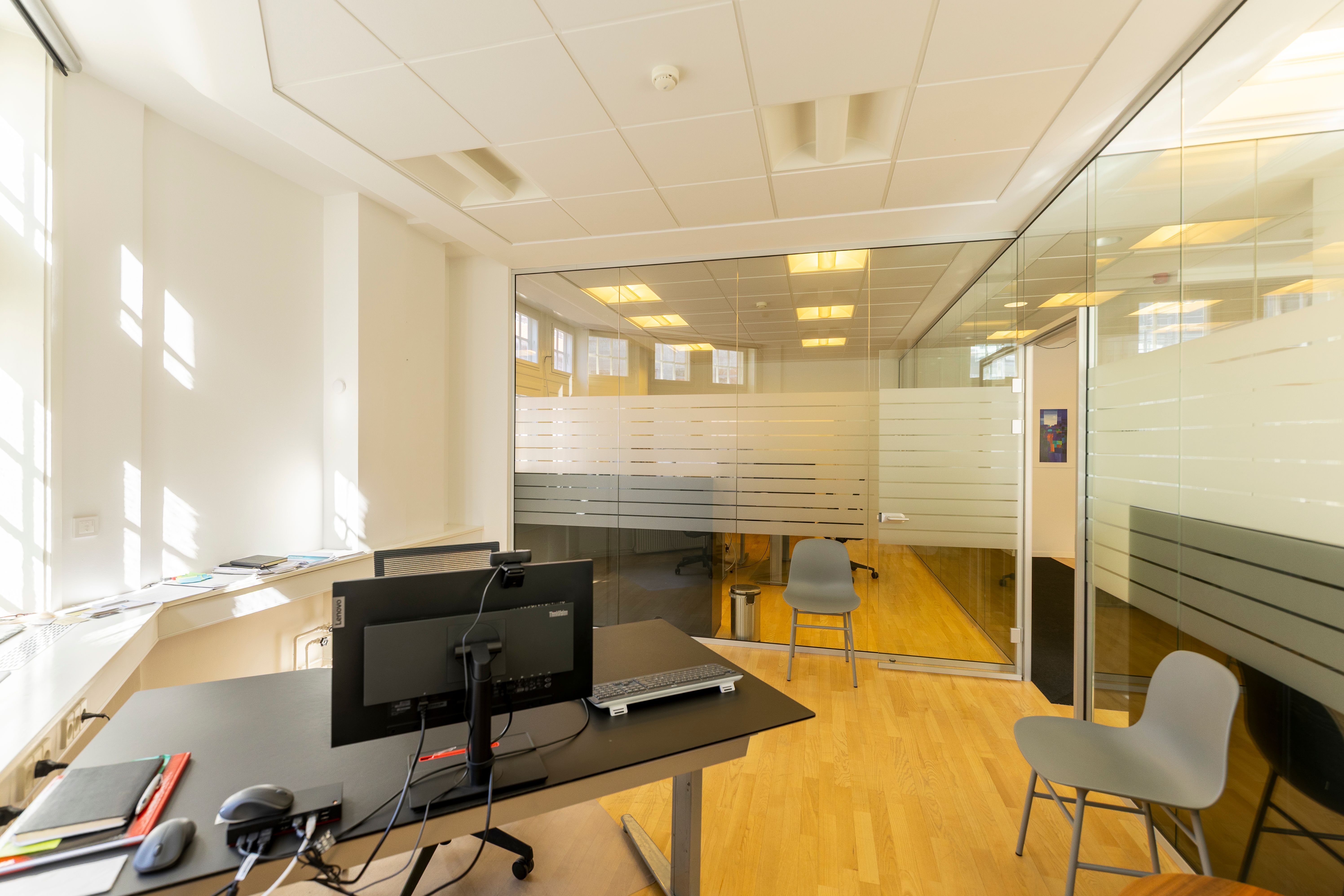 Kontorrum med glasvægge og trægulv, skrivebord med computer, stol og skraldespand, luksuriøs indretning og lysevinduer, eksklusiv beliggenhed nær Kongens Have