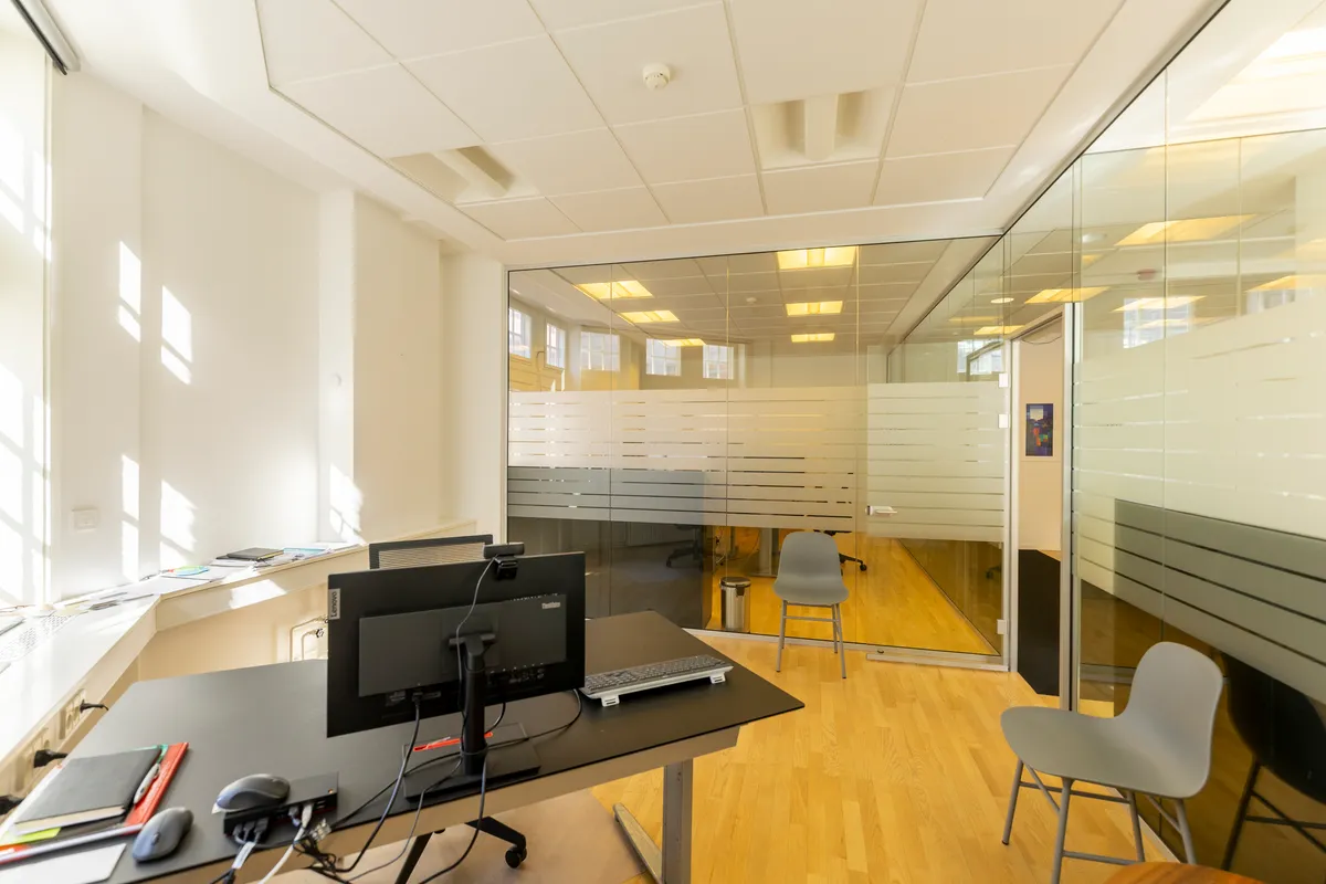 Kontorrum med glasvægge og trægulv, skrivebord med computer, stol og skraldespand, luksuriøs indretning og lysevinduer, eksklusiv beliggenhed nær Kongens Have