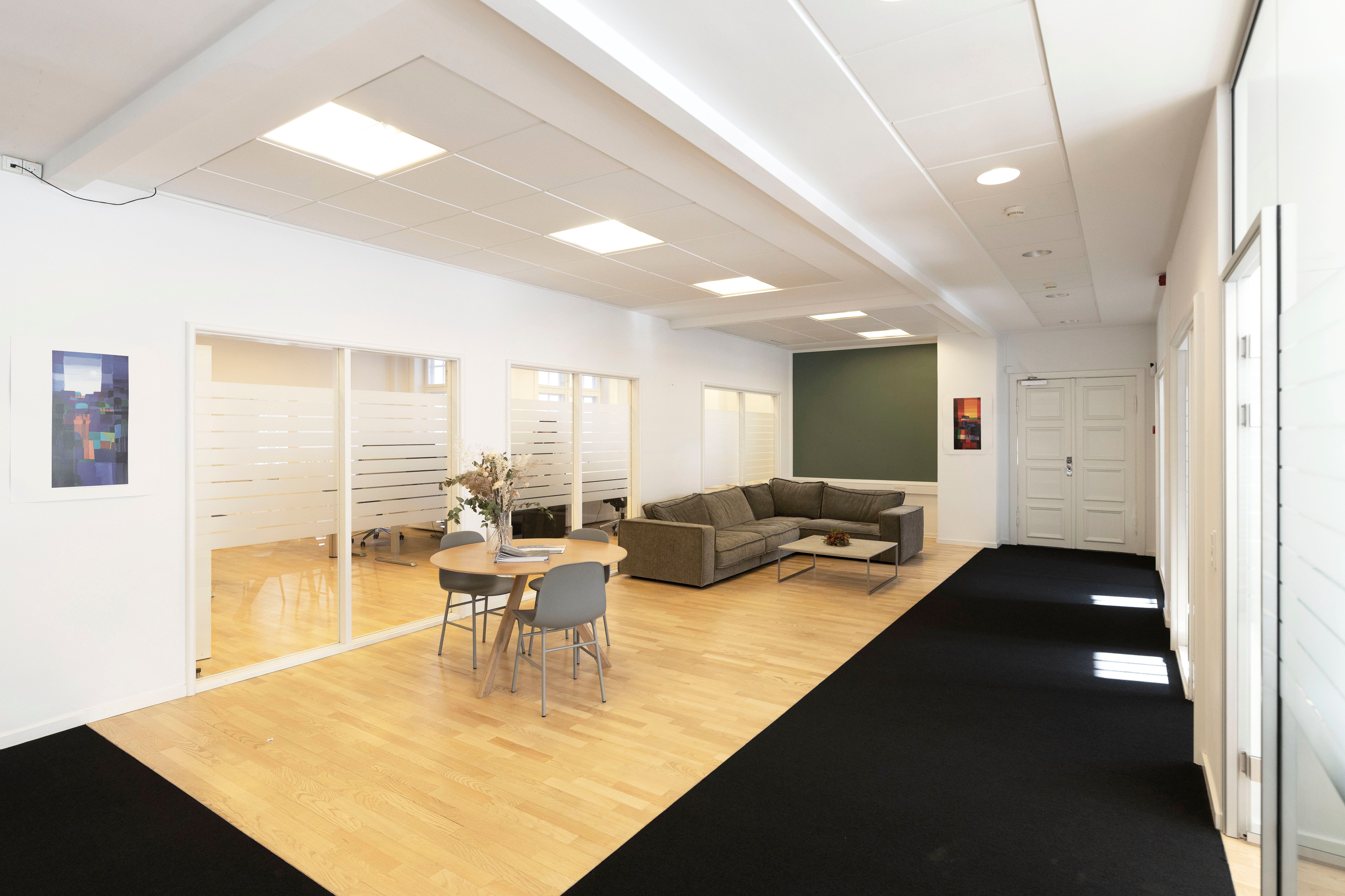 Kontorlokaler med lyse lofter og lysegulve samt møbler og indretning, der skaber et moderne og hyggeligt arbejdsmiljø