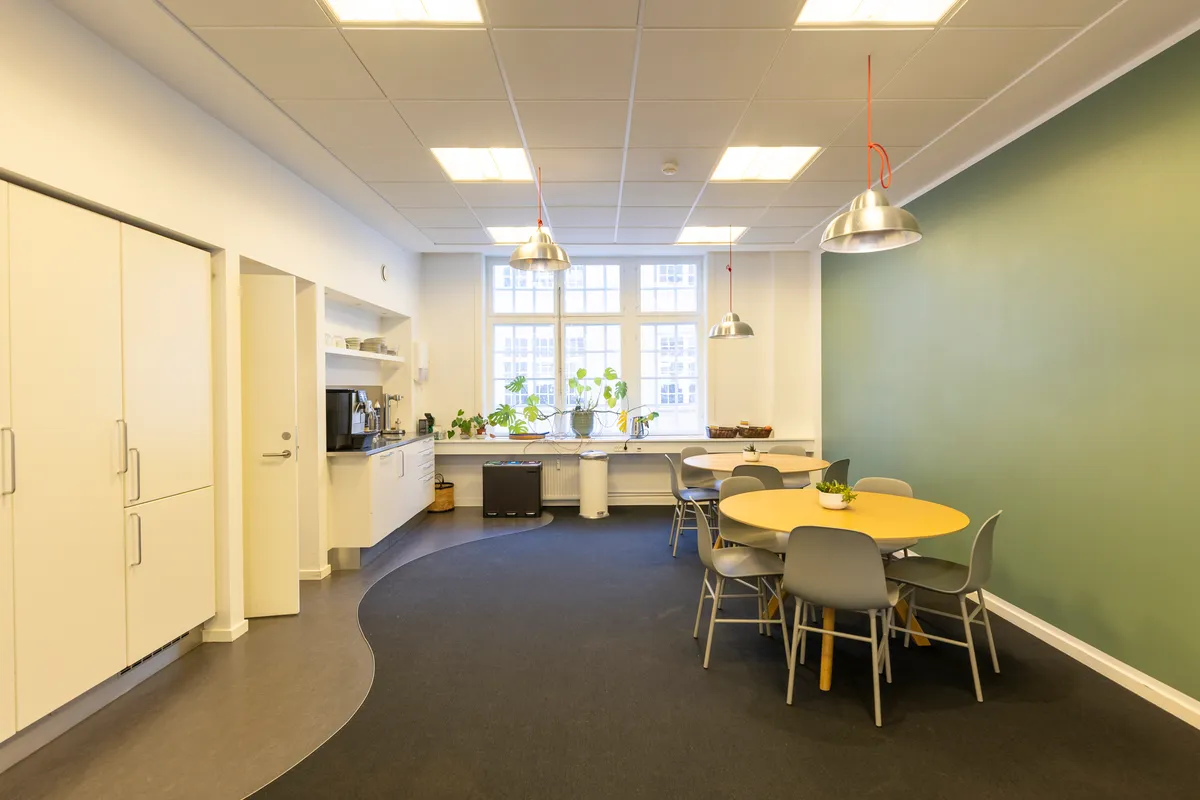 Kanteen i kontoret med plantepotter og møbler med rundt bord, hængelampe og sofaer i kaffepauseområdet med udsigt til Kongens Have.