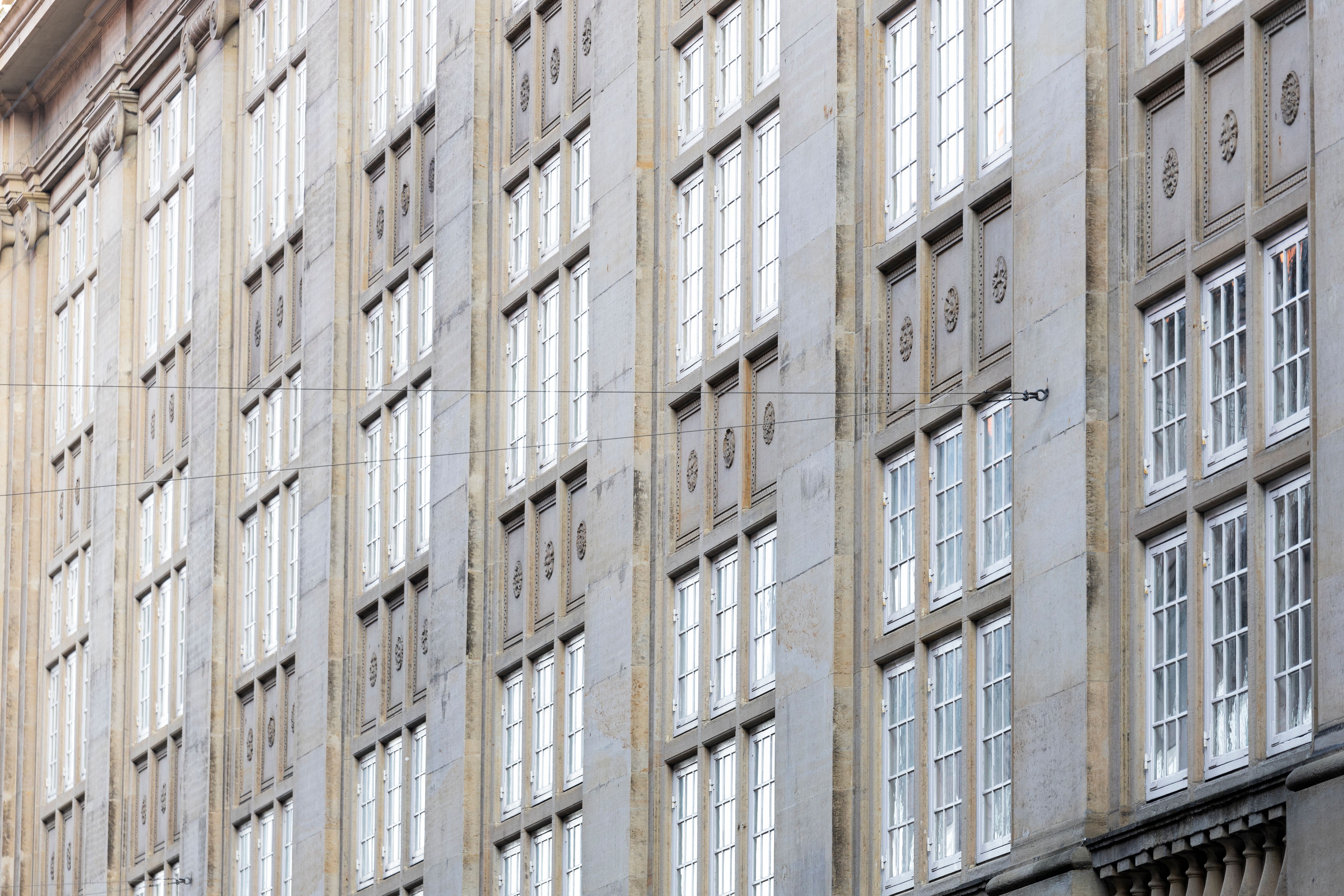 Moderne højhus med mange vinduer og slanke søjler, som vender ud mod en gade med elektriske ledninger og forskelligt udsmykning