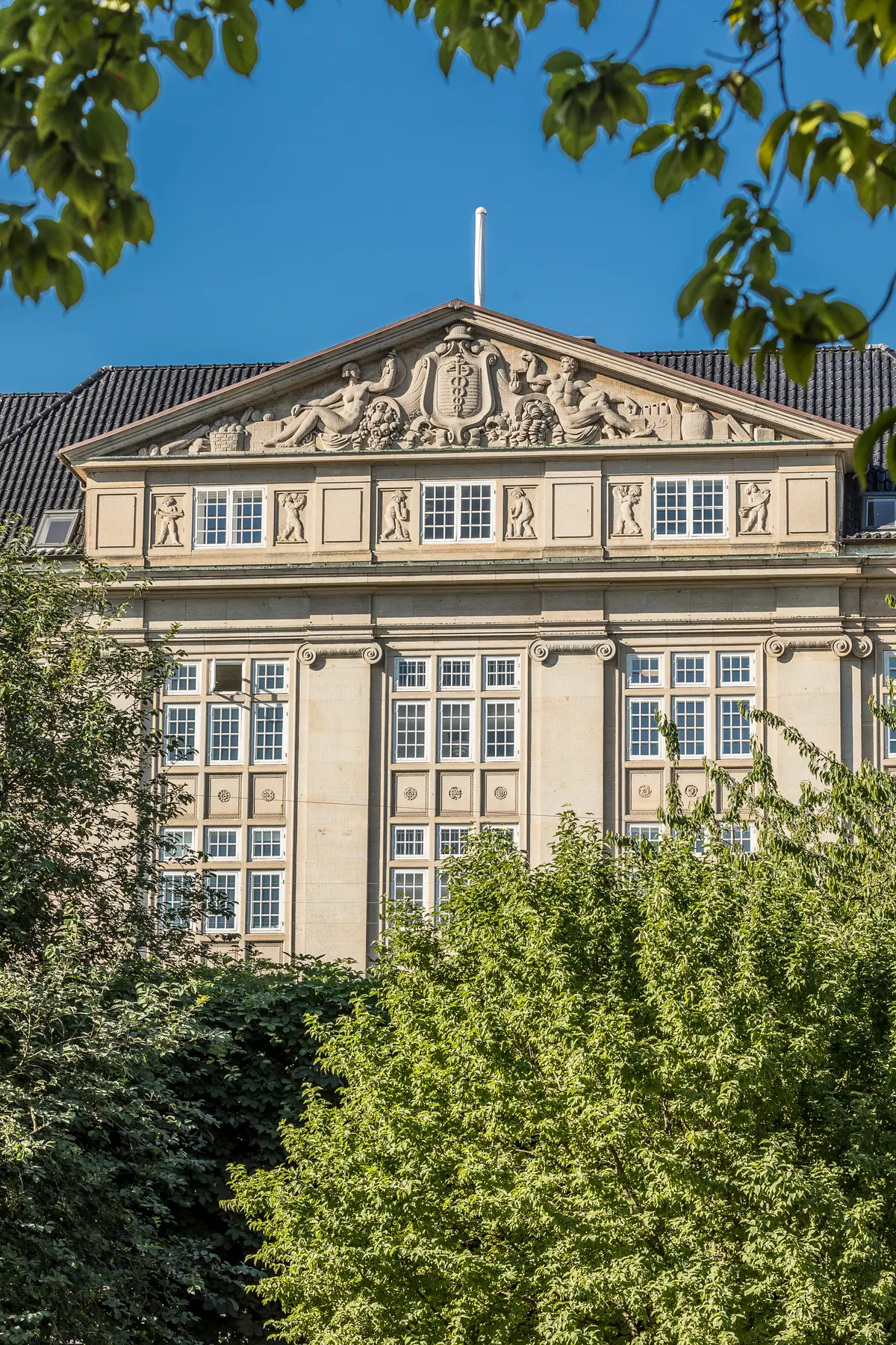 En stor, historisk bygning med skulpturer, mange vinduer og en terrasse med udsigt over Kongens Have. Elegant hovedindgang med statuer og søjler