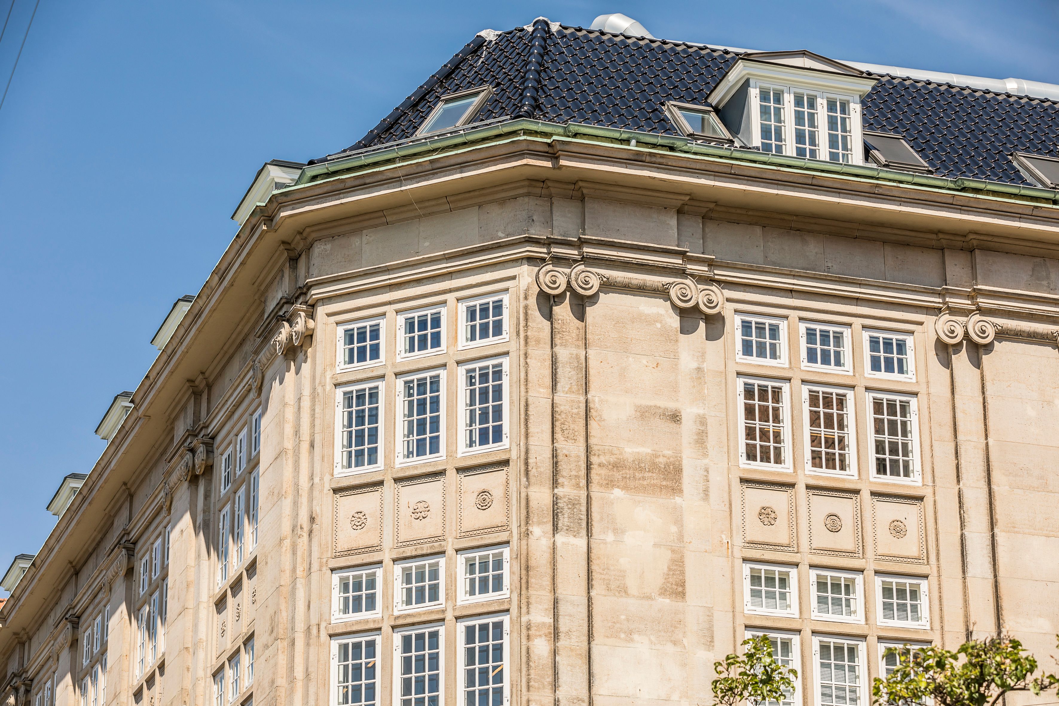 Detaljeret udsigt på en historisk bygning med kæmpe vinduer og smukke, dekorative ornamenter i gult murværk. Fælles kantine og smukke kontorlokaler i Møntergården i København.