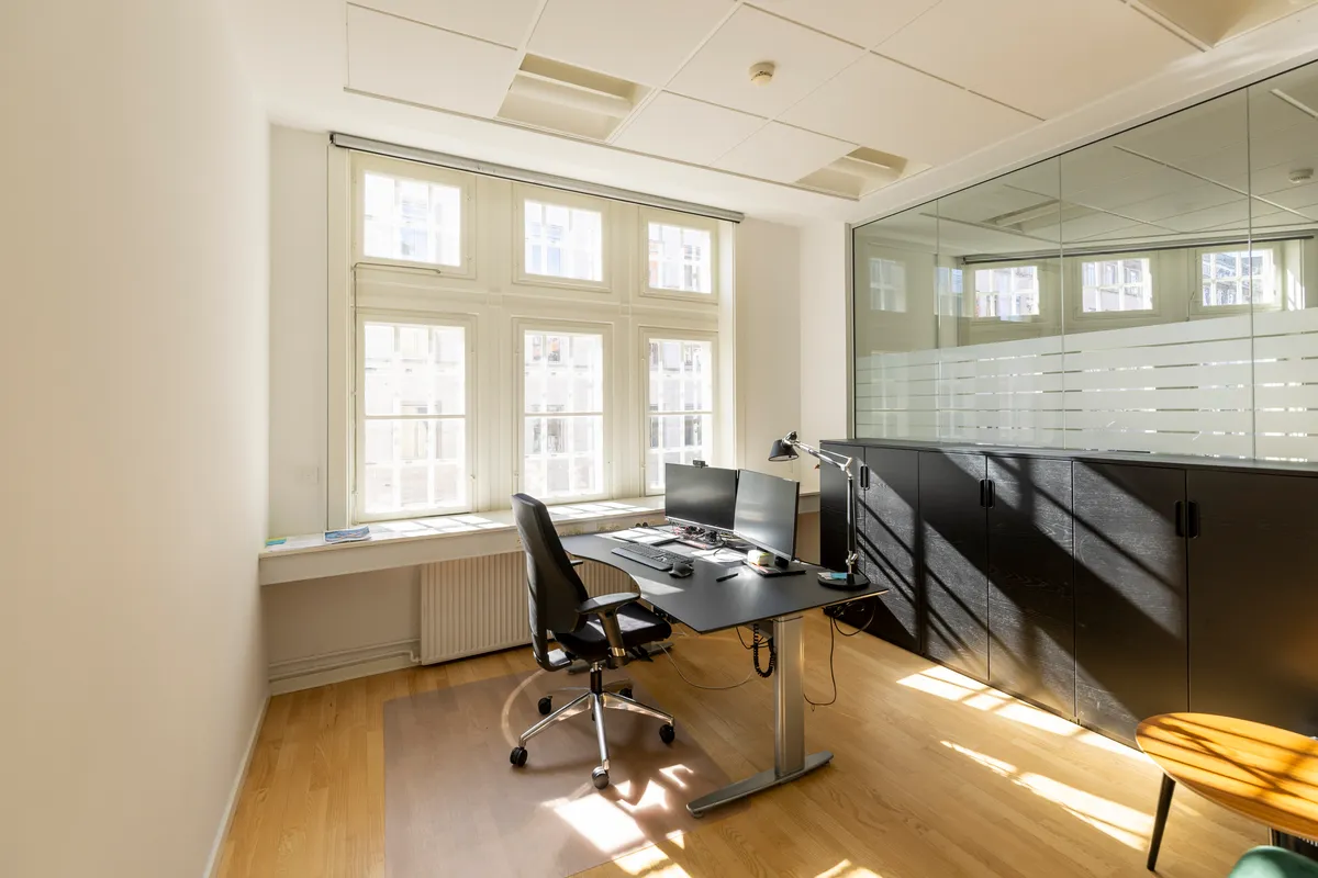 Kontor med vinduer, skrivebord, 2 skærme, lampe, sort høj kabinet, gulvlampe, trægulv og træbord