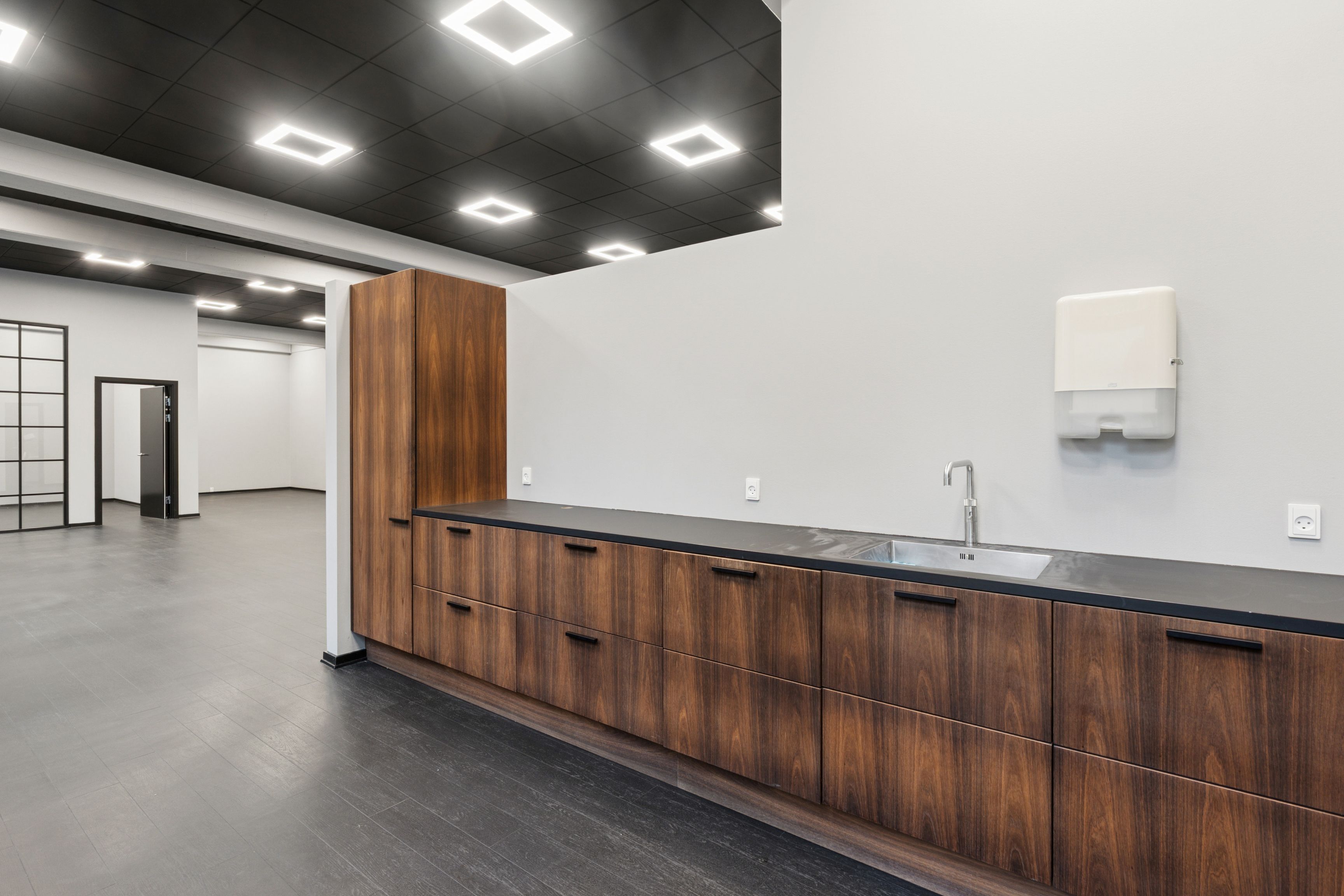 Højloftet kontorhus med lyse loftslamper og mørke lofter. Højloftet lokale med høj kvalitet og lyse gulvbelægning. Væg og lofter er hvide og mørke.