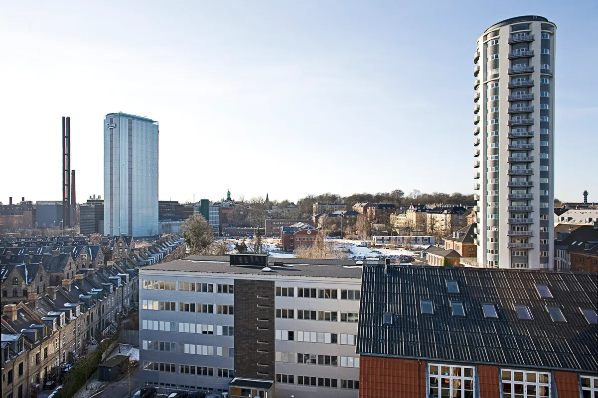 Stort kontorhus med facader i glas og rød mursten. Forskellige bygninger med forskellige højder og stilarter. Bygninger med røde tagdækninger og glasvinduer. Sne dækker jorden og træerne