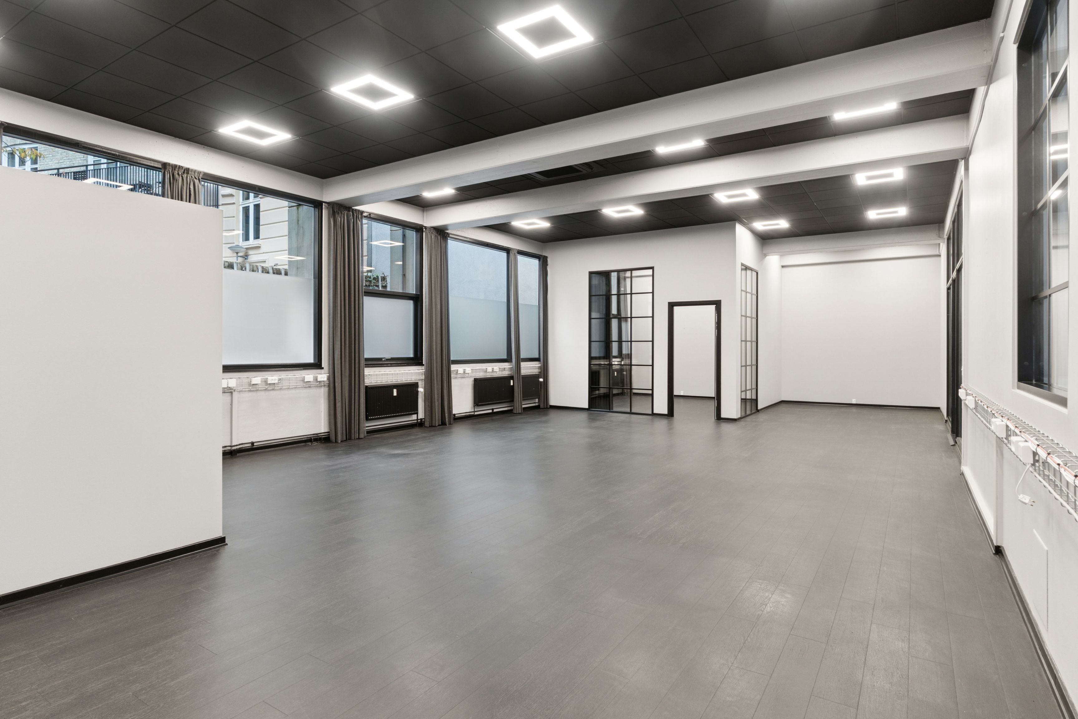 Højloftet kontorrum med lysegult gulv og hvide vægge, store vinduer og moderne lamper. Minimalistisk interiør med moderne design. Lyst og åbent rum med gode tage og store vinduer