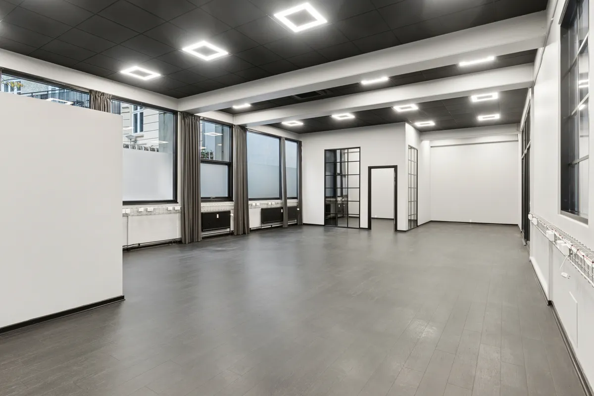 Højloftet kontorrum med lysegult gulv og hvide vægge, store vinduer og moderne lamper. Minimalistisk interiør med moderne design. Lyst og åbent rum med gode tage og store vinduer