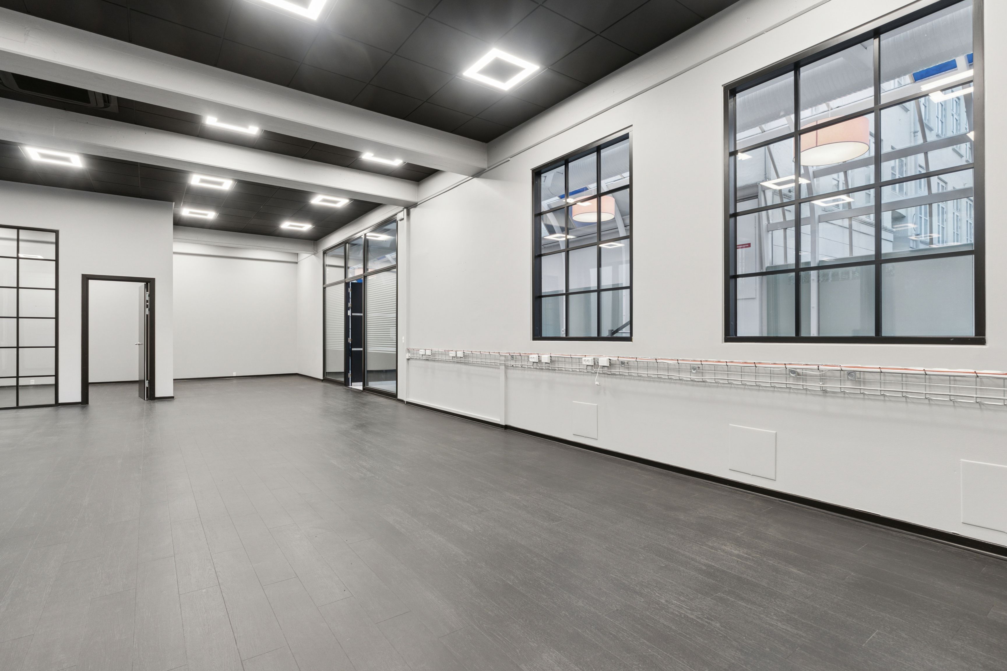 Stor, højloftet lejemål med glasvinduer og trægulv på Vesterbro. Plads til kontor eller showroom med hvide vægge og mørke loftsbjælker.