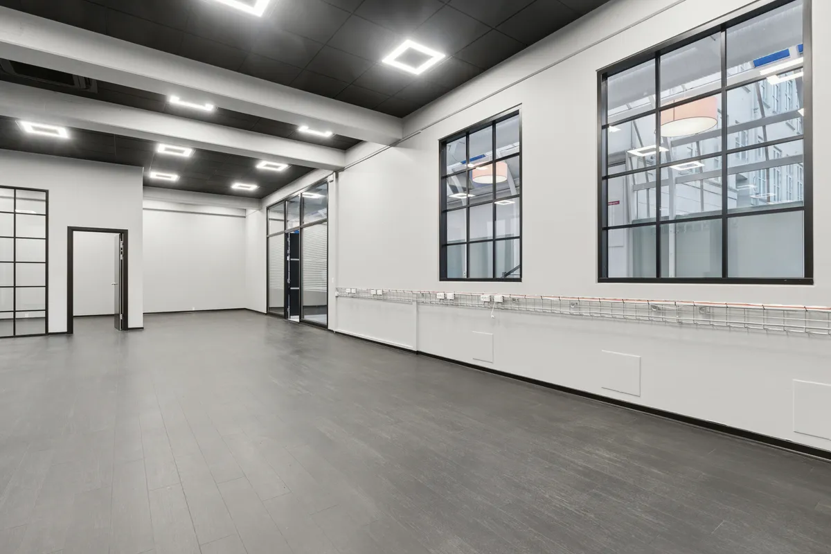 Stor, højloftet lejemål med glasvinduer og trægulv på Vesterbro. Plads til kontor eller showroom med hvide vægge og mørke loftsbjælker.